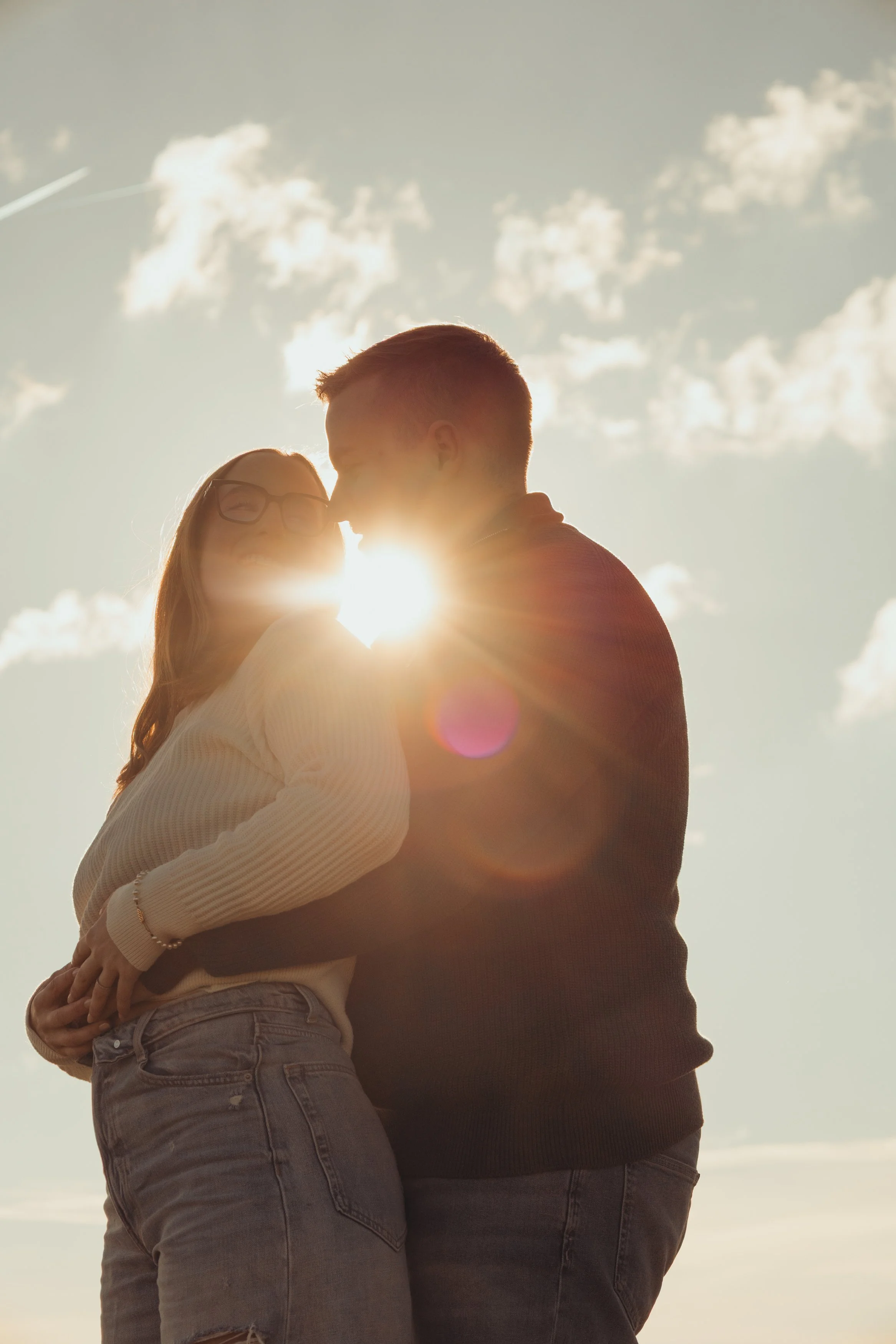 Un couple qui s'embrasse sous un ciel ensoleillé avec des nuages blancs.