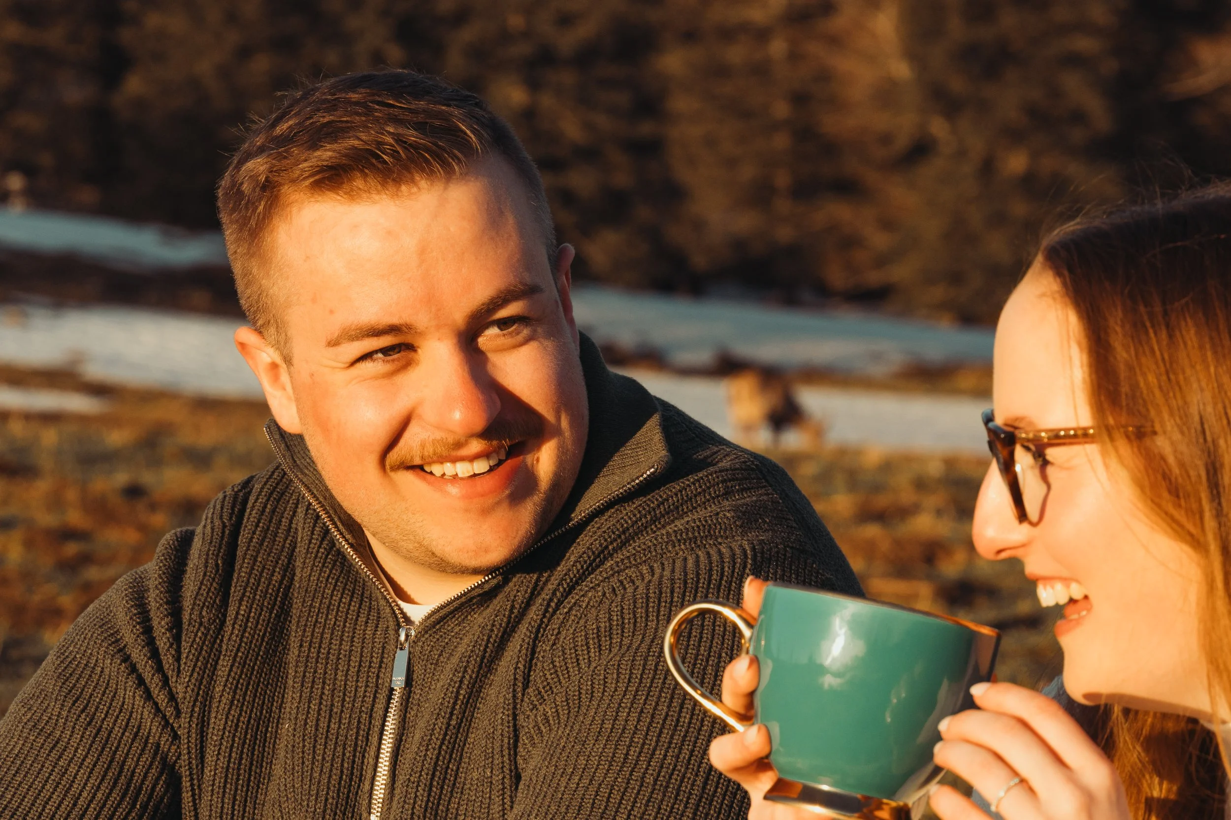 Deux personnes souriantes, un homme et une femme, regardant un téléphone portable ensemble en plein air au coucher du soleil, avec un fond de nature rocheuse.