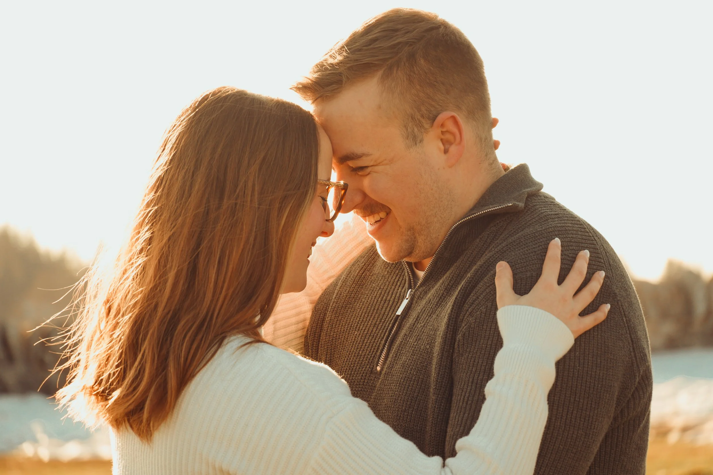 Un couple souriant, avec la tête proche, lors d'un moment tendre en plein air au coucher du soleil.