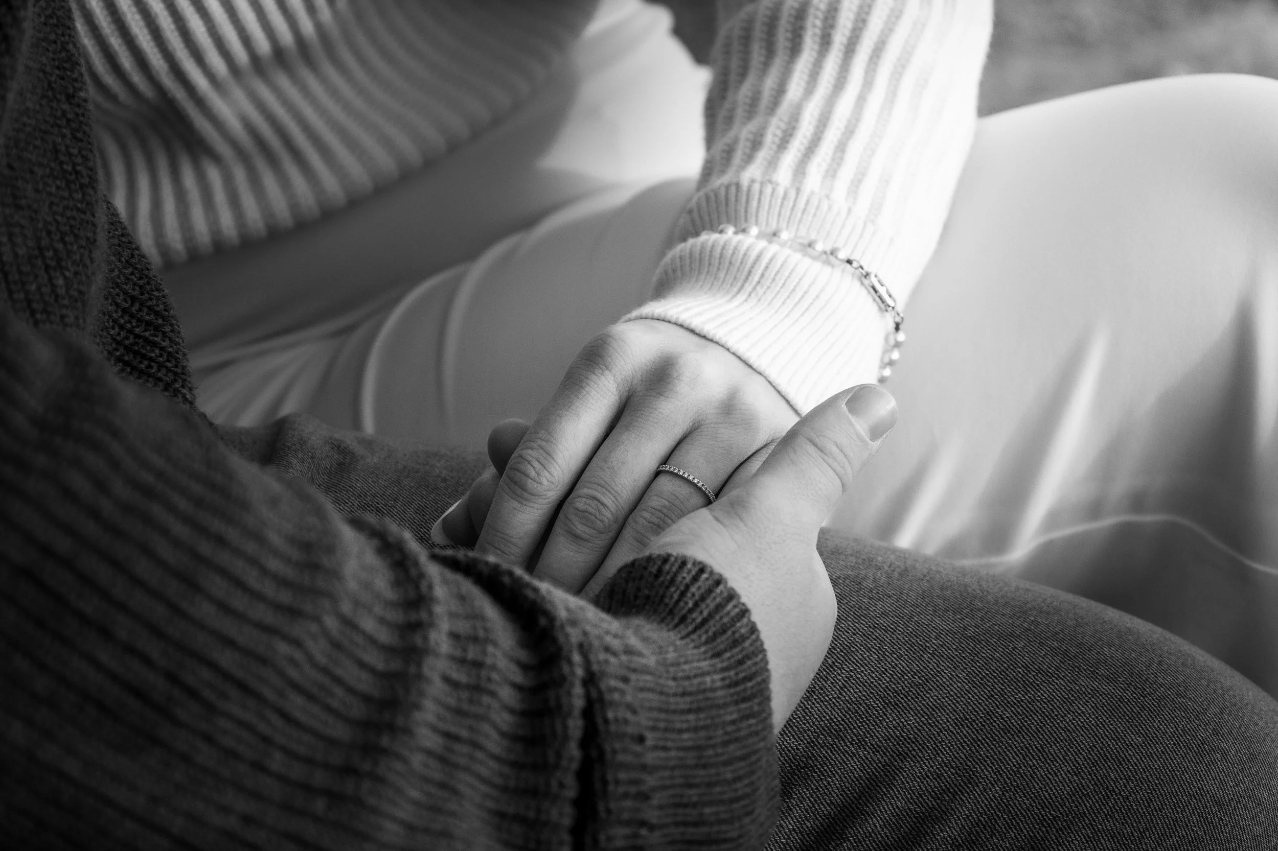 Une personne tient la main d'une autre personne, les deux portent des vêtements en tricot, en particulier des manches en ras du cou. La photo est en noir et blanc.