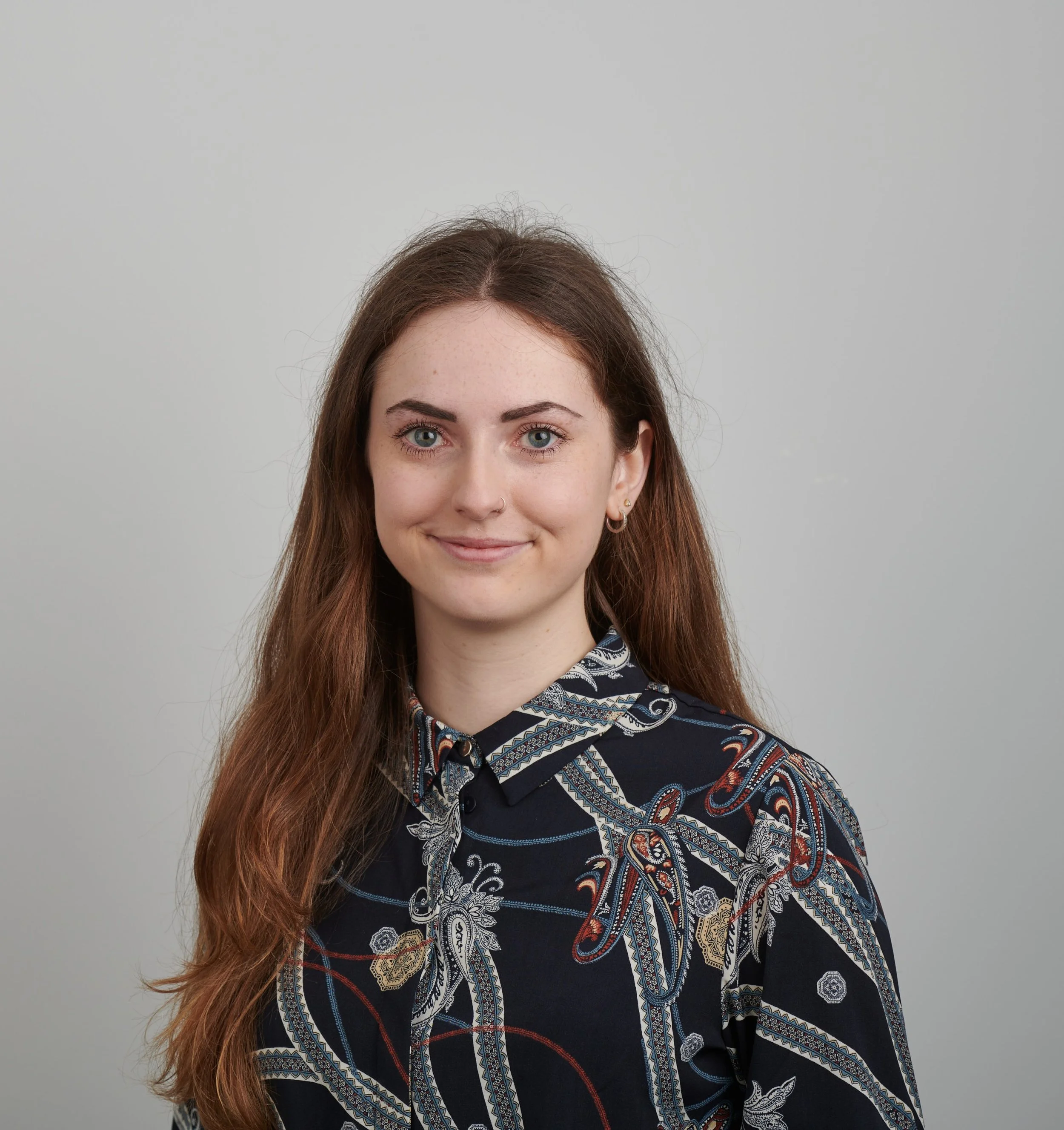 Photo of Emma Baker smiling with long auburn hair, wearing a black & white floral blouse.
