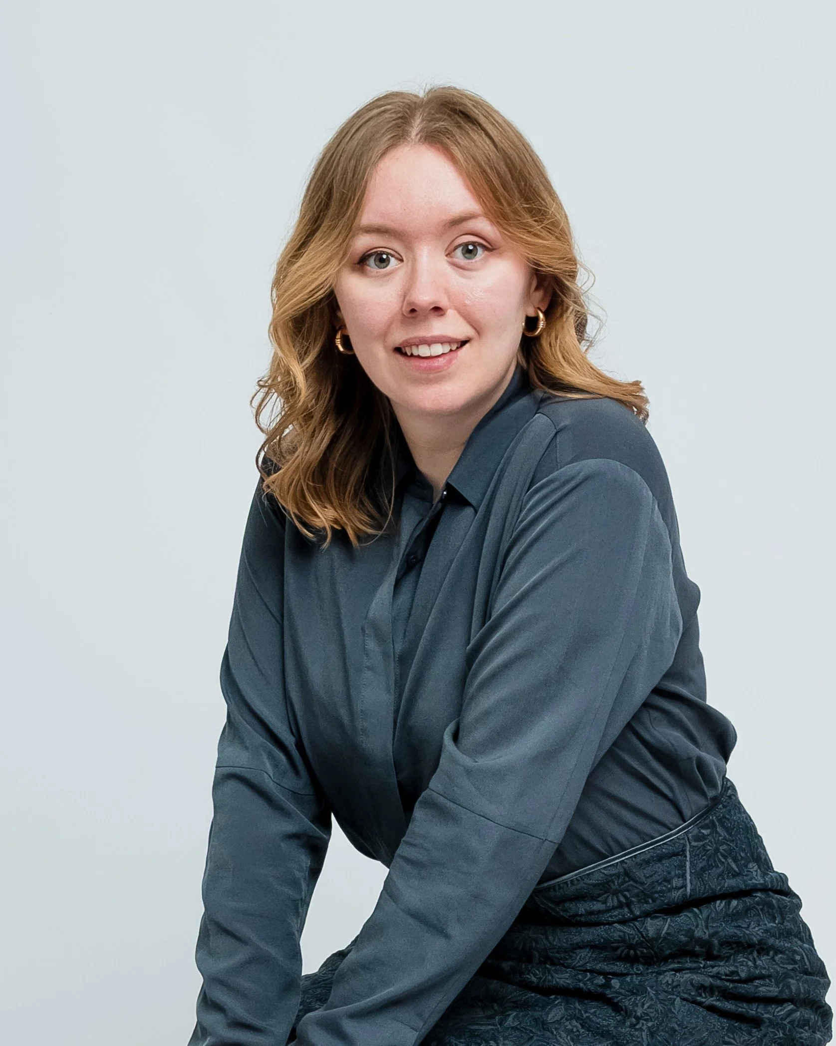 Photo of Rebecca Farthing, a young woman with long wavy brunette hair smiling and leaning forwards.