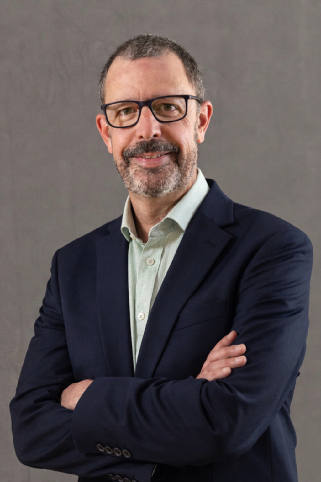 Image of Phil Canale who has short dark hair, wears dark glasses and has a greying beard. He is smiling with his arms folded wearing a shirt and jacket.