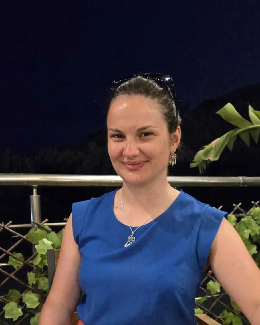 Photo of Alice Edwards, a young woman with brown hair tied back, smiling wearing a bright blue top.