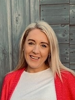 Photo of Charlotte Leighton smiling with shoulder length blond hair wearing a white top and red cardigan