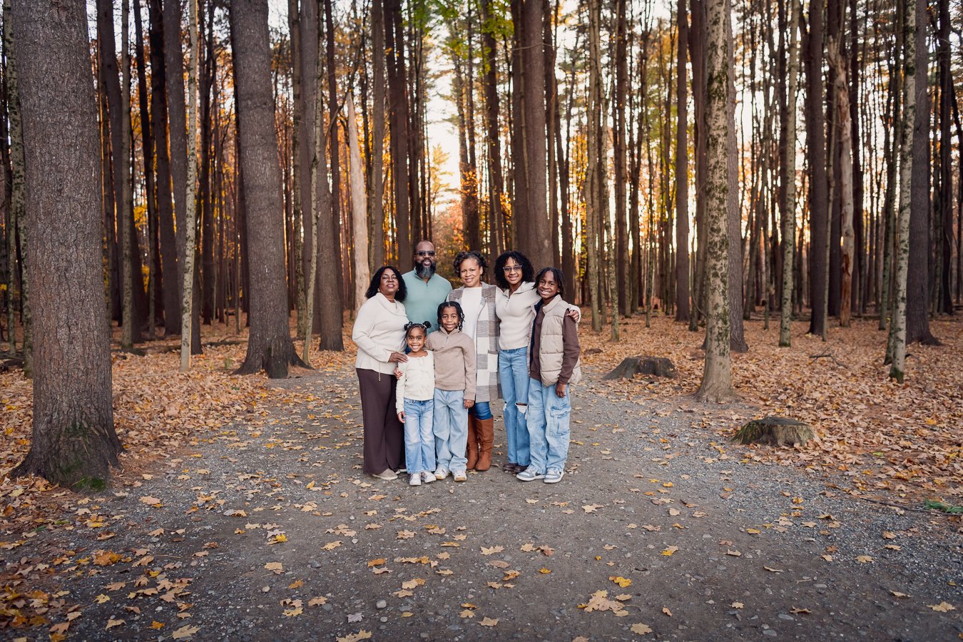 Family of seven standing on a dirt path in a forest with fall leaves, during sunset.