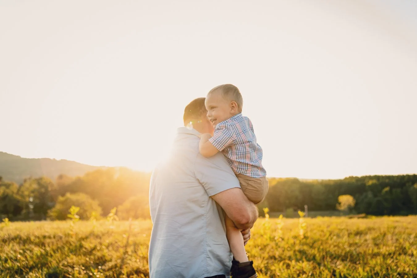 A man holding a young boy in an open field during sunset, smiling and enjoying the moment.