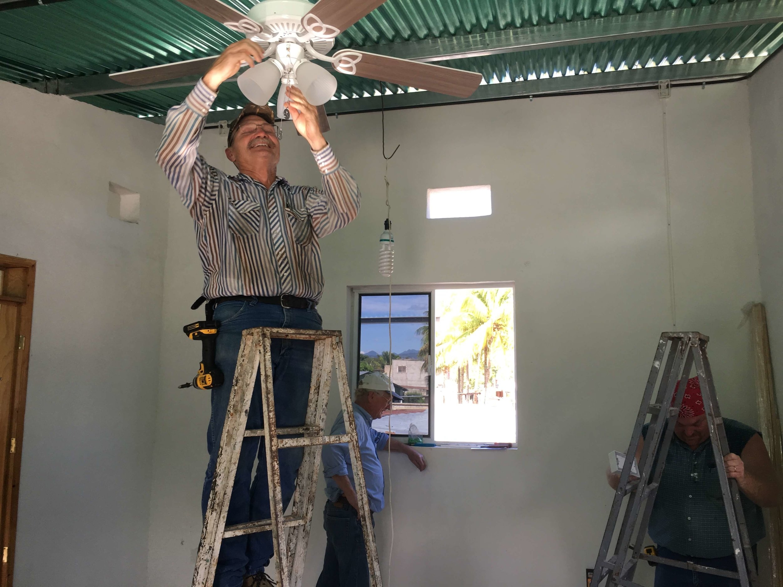 Mark Green finishes installing a ceiling fan while brother Lance fiddles with a ladder and friend Bill Buchanan looks out the second story window to admire the view. 