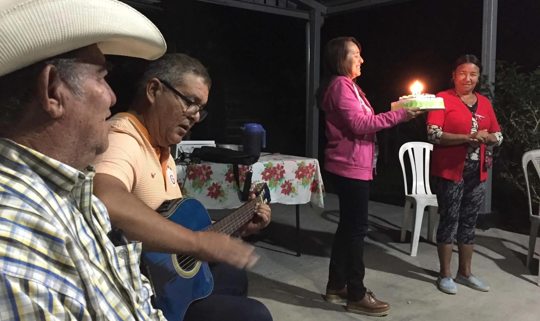 In a PSE group in Santa Rosa de Lima, Cesar looks on as Humberto plays a birthday song on his guitar while his wife Enma brings out a birthday cake for a member of their group.