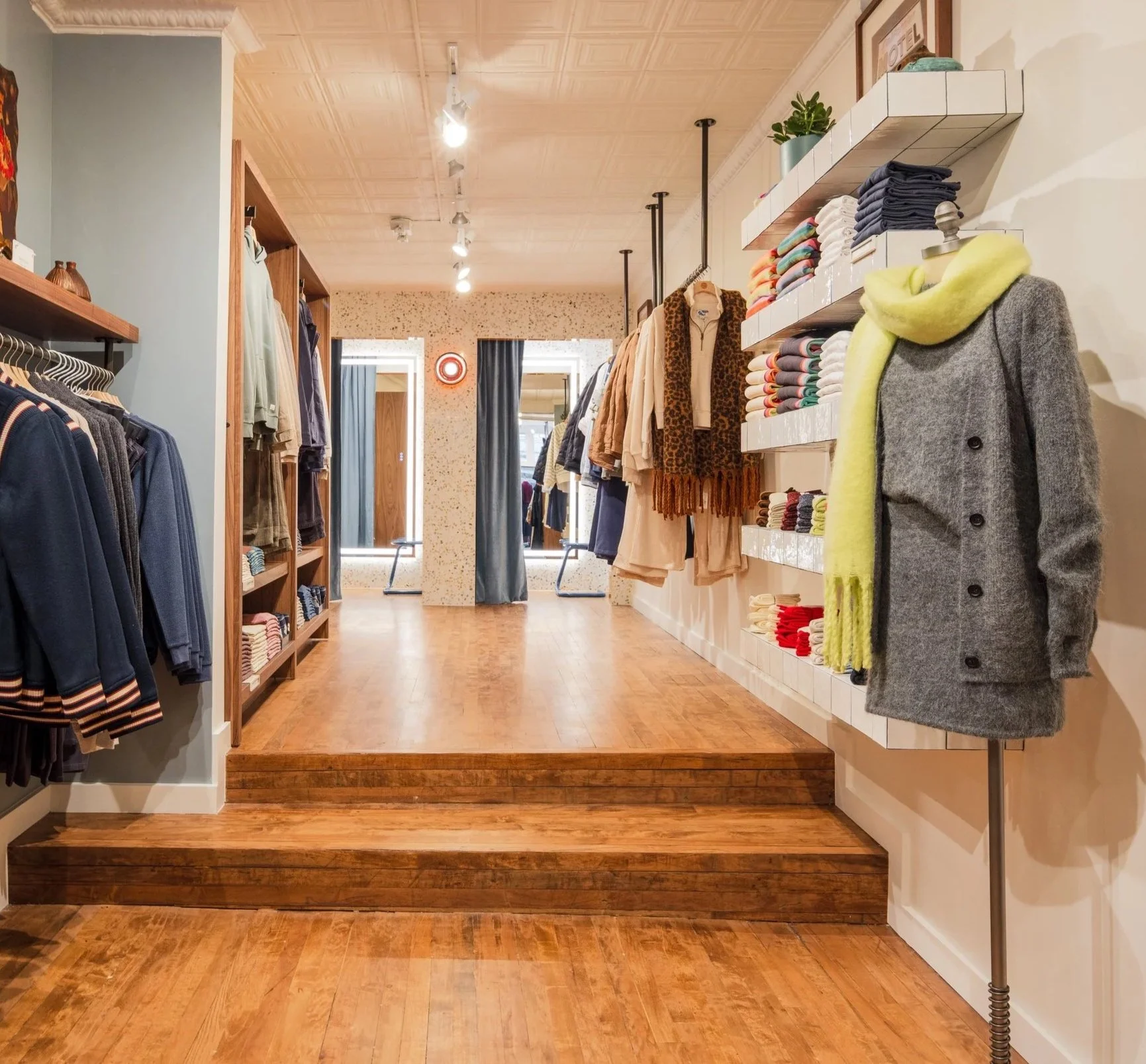 Interior of a clothing store with wooden floors, displaying jackets, sweaters, and scarves on racks and shelves.