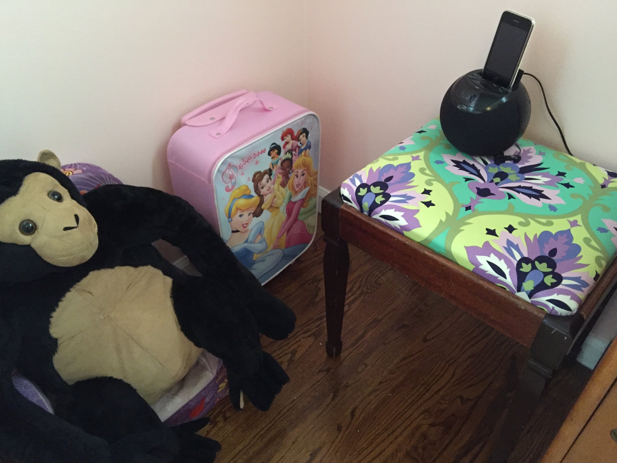 Next to the cubby shelf in this corner of the room is her squishy chair being used by her pet gorilla, her princess suitcase full of dolls, and a little stool that I recovered in a fun fabric. Stool/Bench: Garage sale; Suitcase: From my SIL