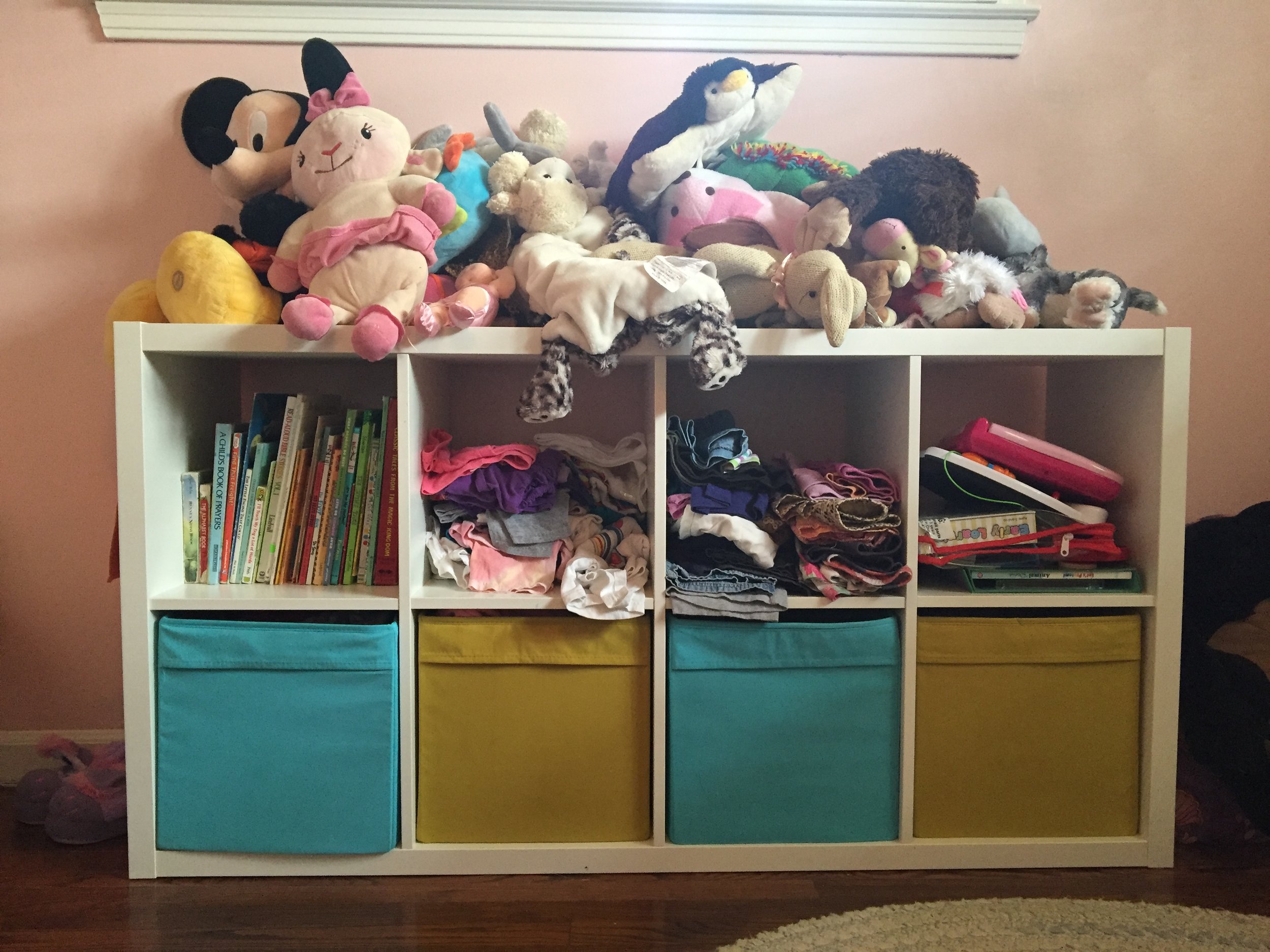 Books, clothes (they look like a big mess, but they're actually organized for Meena, so she knows where everything is) in the middle two top cubbies, and toys in the last. The bottom bins are more clothes organized for her. I have everything separated out so that she can get her own clothes out easily and dress herself. No dresser with heavy drawers that can fall out on her. Everything is perfect for her height. And this shelf is perfect for throwing her zoo of stuffed animals up on.