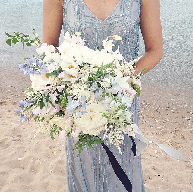 I am a lady of many, MANY words; however, I’ve yet to find the ones to express just how LOVELY I find this arrangement by Hey Gorgeous Events . Following a calm and predominately monochromatic color palette really allows for the infrequent POPS of pastel pink and blue to steal the show! Moreover, with white roses and a variety of greenery, this ethereal bouquet is truly fairytale-worthy! (Photo by Nancy Ray Photography!)