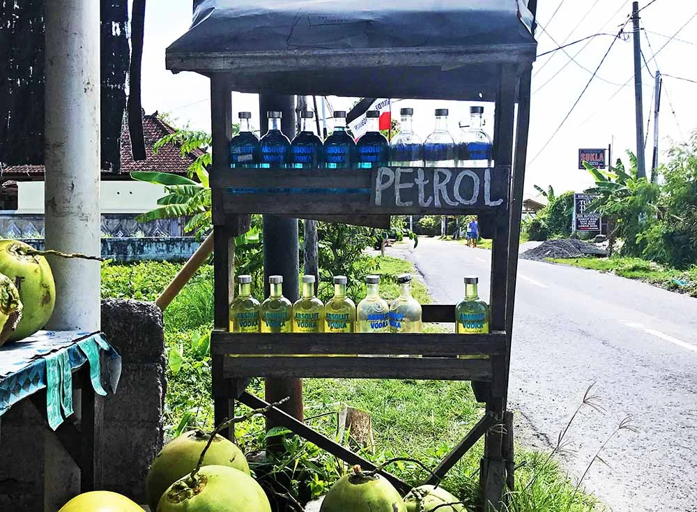 A road side petrol (gasoline) vendor. Notice the whole fresh coconuts also for sale!