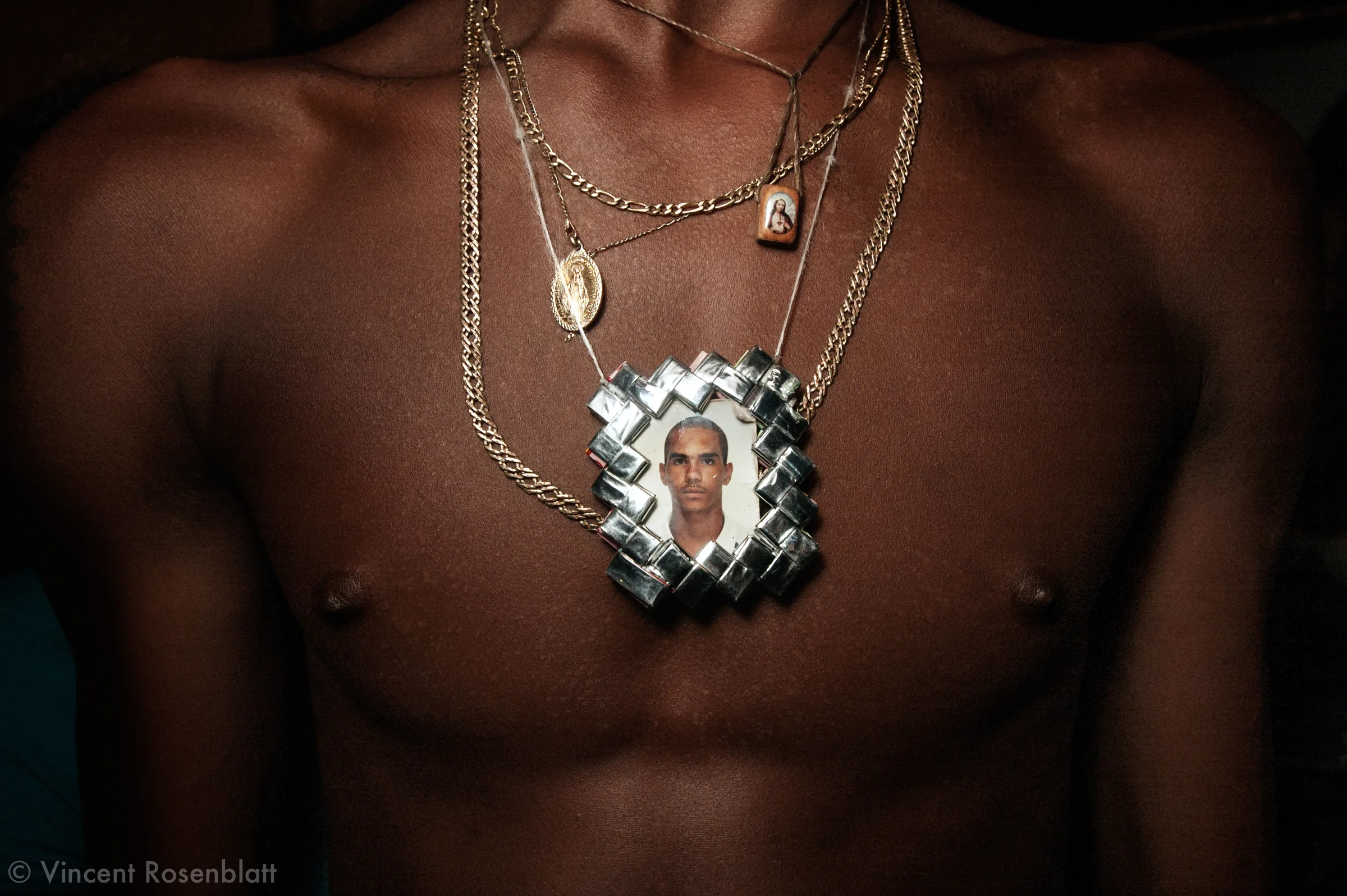 Pendant representing a deceased friend. Baile Funk in Morro do Turano slum. Rio de Janeiro, 2006..The Funk carioca movement is fashion and look as well : The boys show off their muscles and naked torsos, adorned with chains and tattoos, accessories which will make the difference during the ball. Girls will look after their bikini marks, which will appear above mini-skirts or micro-shorts. Everything is worth to draw attention! .