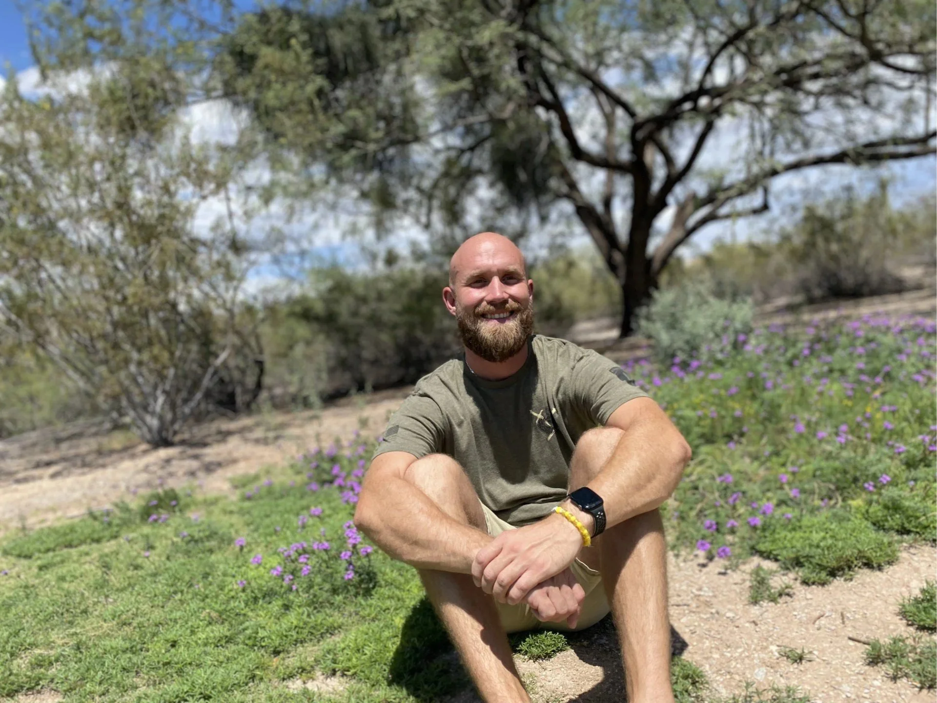 Shane Myers sitting in the desert amongst some Goodding's verbena