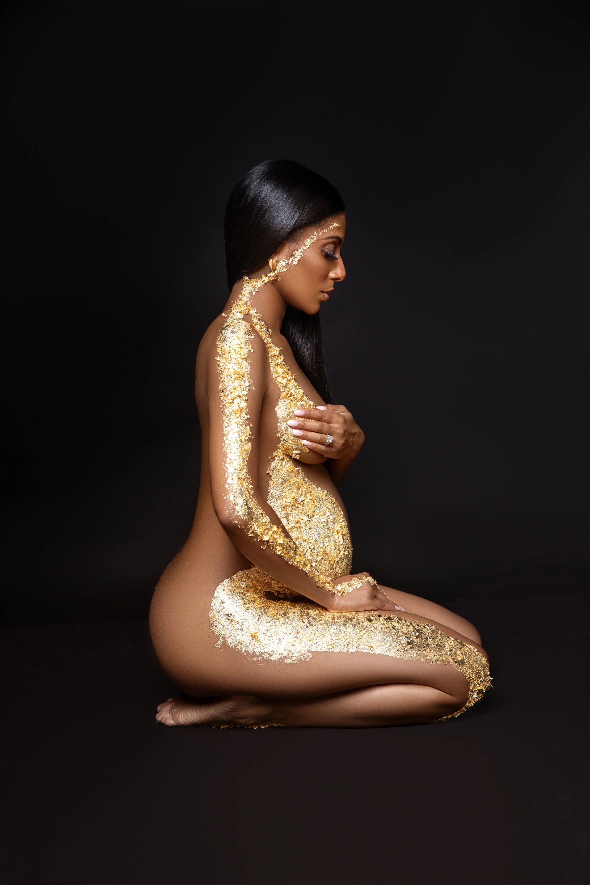 Maternity body art photography featuring gold leaf accents on the pregnant form.