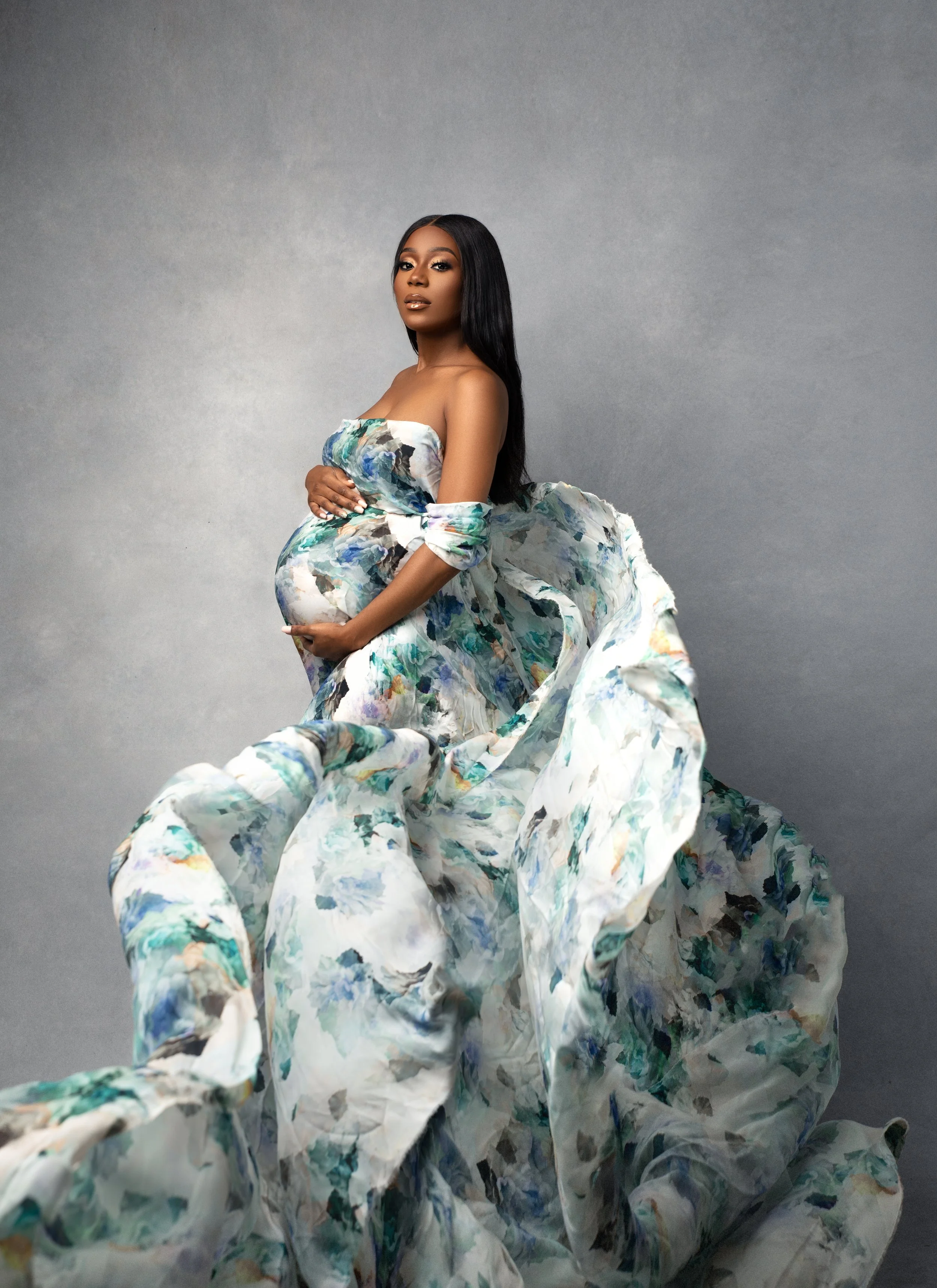 Elegant maternity portrait of a pregnant woman wrapped in blue floral silk draping inside a full-service Brooklyn NYC maternity photography studio.