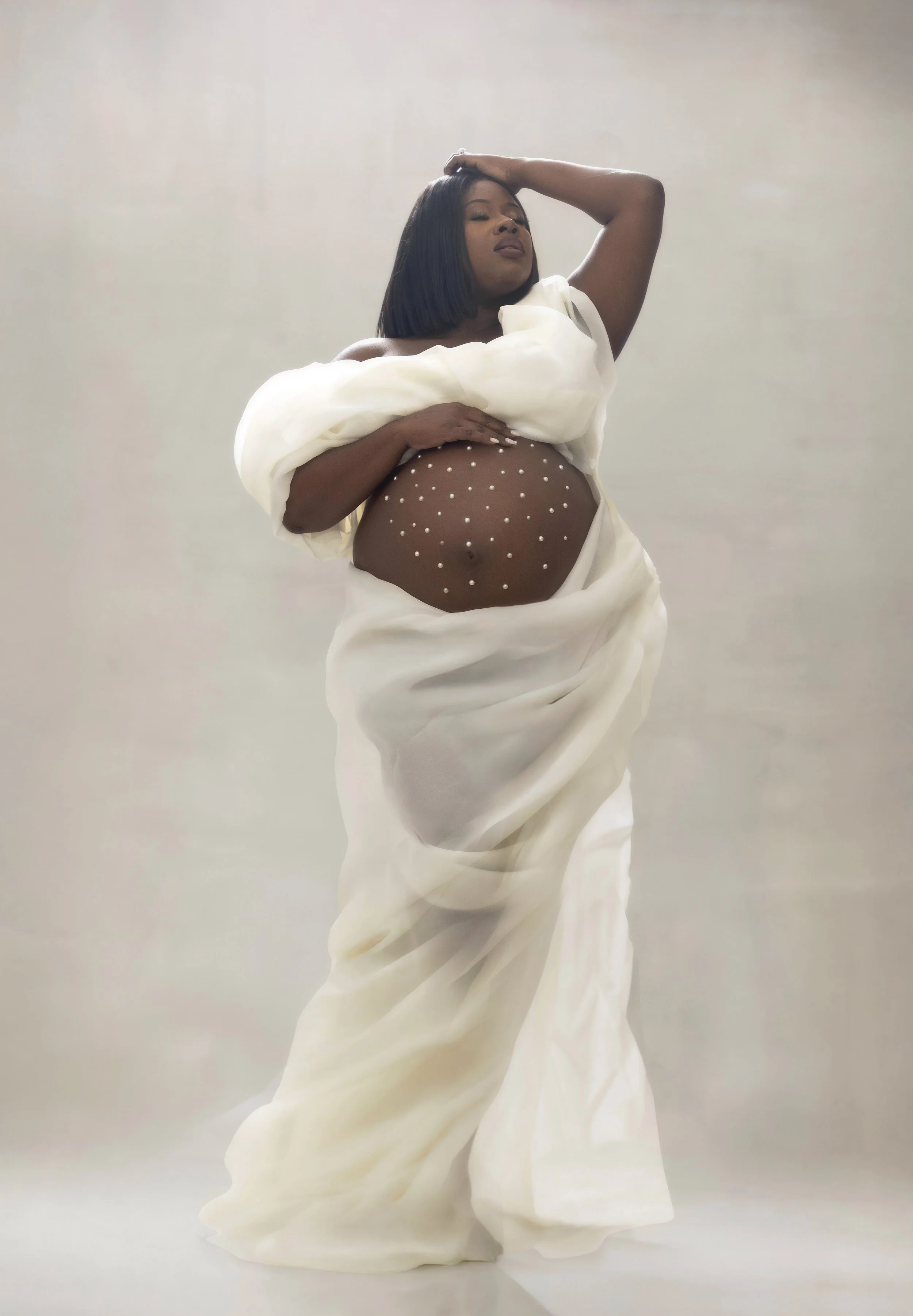 Pregnant Black woman wrapped in white fabric with pearl-adorned baby bump, luxury maternity portrait, Candace Howe Studios Brooklyn NYC