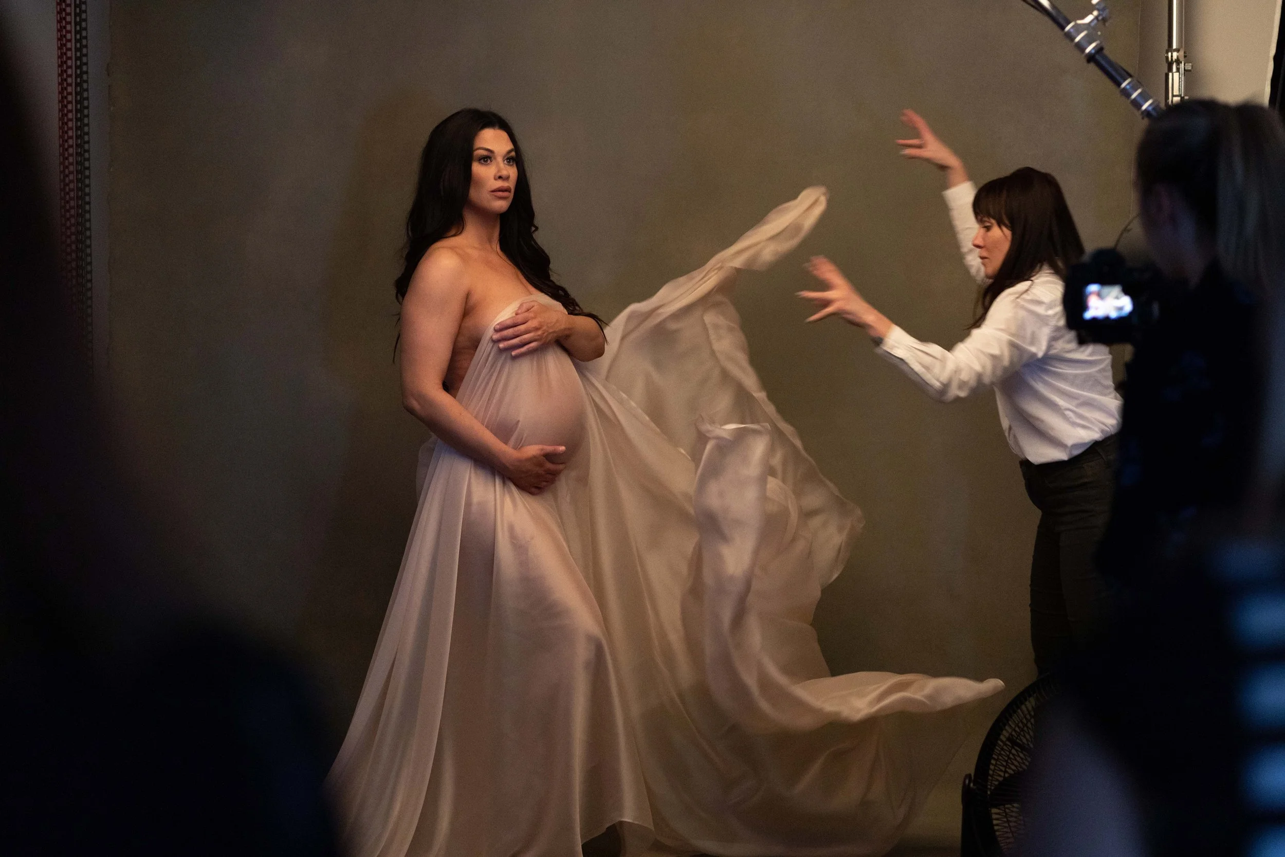 Behind-the-scenes maternity session in a Brooklyn studio with flowing silk draping creating soft movement around an expectant mother.
