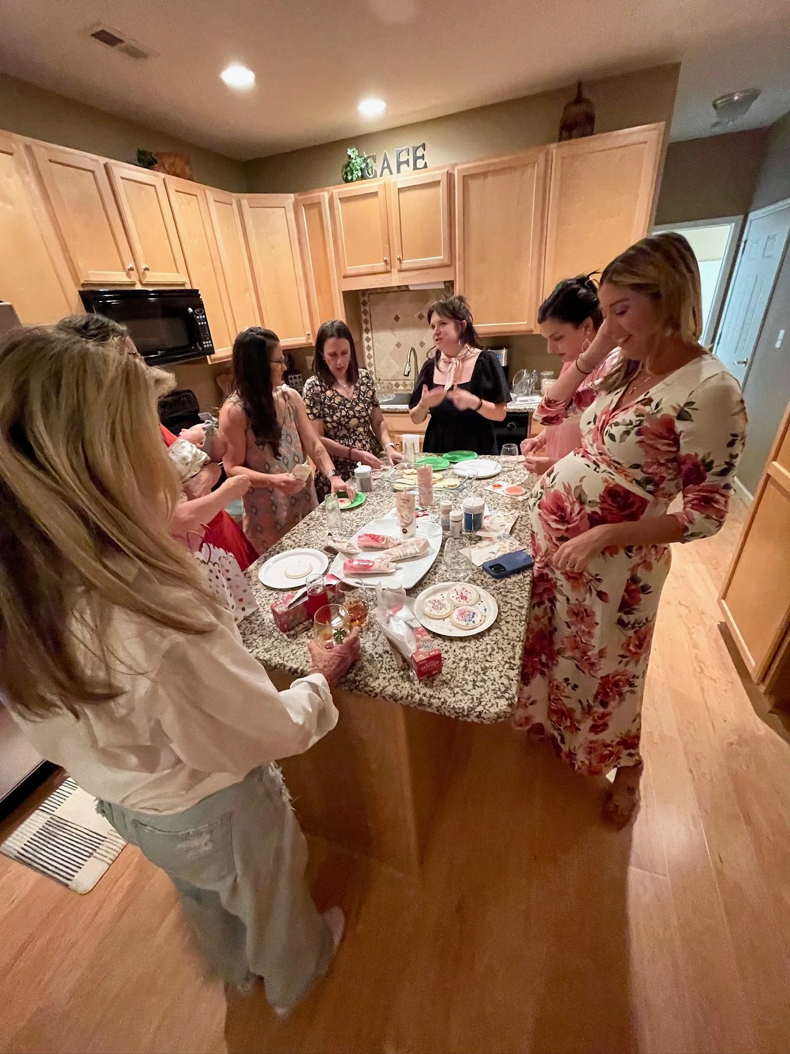 Group of women gathered around a kitchen counter, preparing food and chatting in a cozy home setting.
