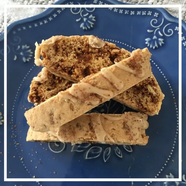 A rustic plate of coffee, Skor and almond biscotti drizzled with coffee glaze, showing crisp golden edges and caramel toffee bits, served alongside a cup of hot coffee on a warm wooden surface.