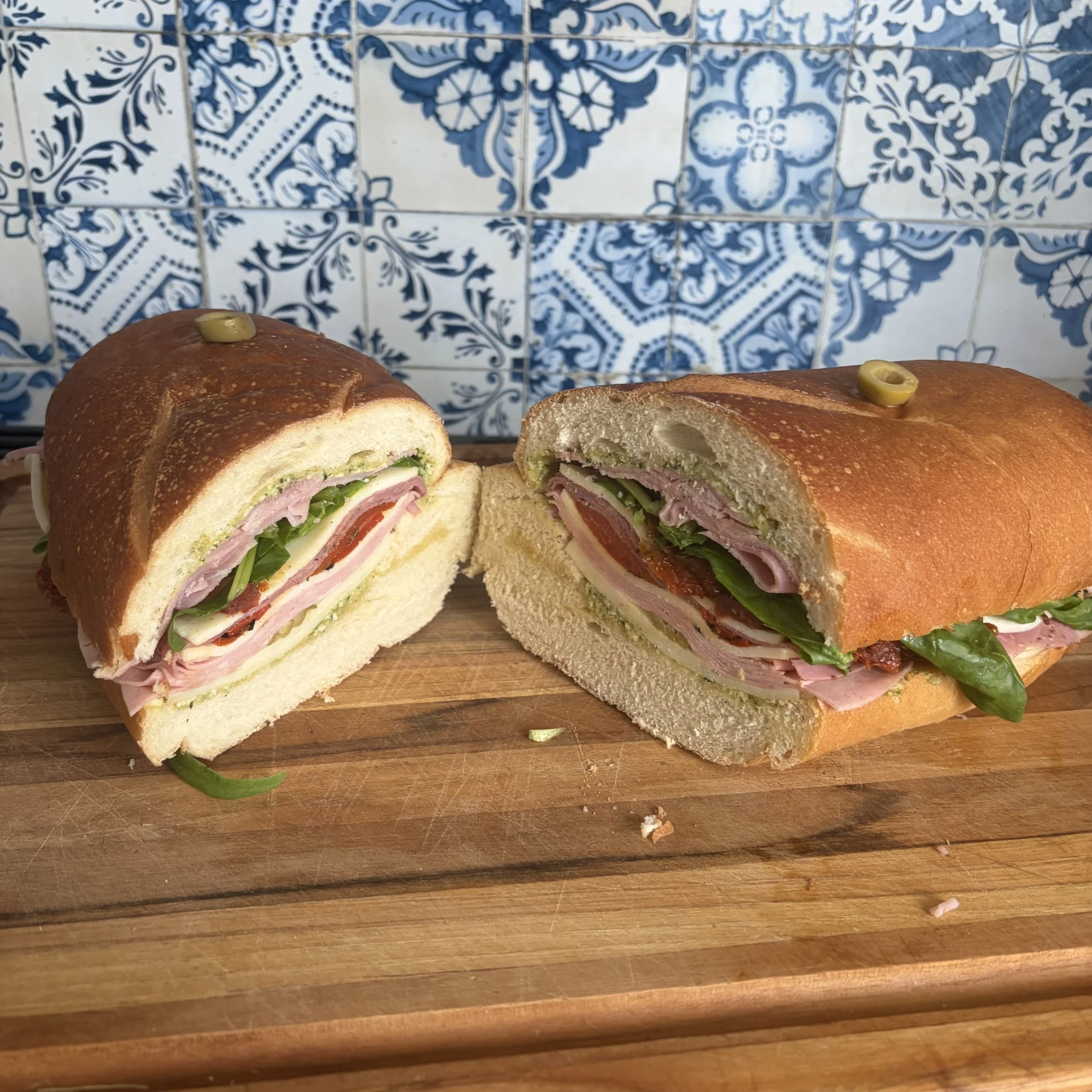 Close-up of giant Italian party sandwich showing layers of prosciutto, salami, provolone, roasted peppers and pesto inside crusty loaf