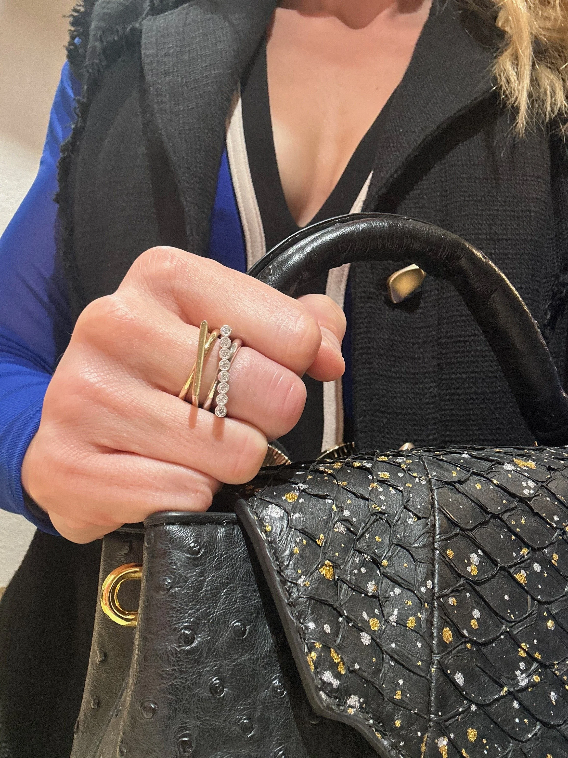 Blonde models Crossroads x-style rings in 18k yellow gold and silver with diamonds while clutching a gold and silver speckled handbag.