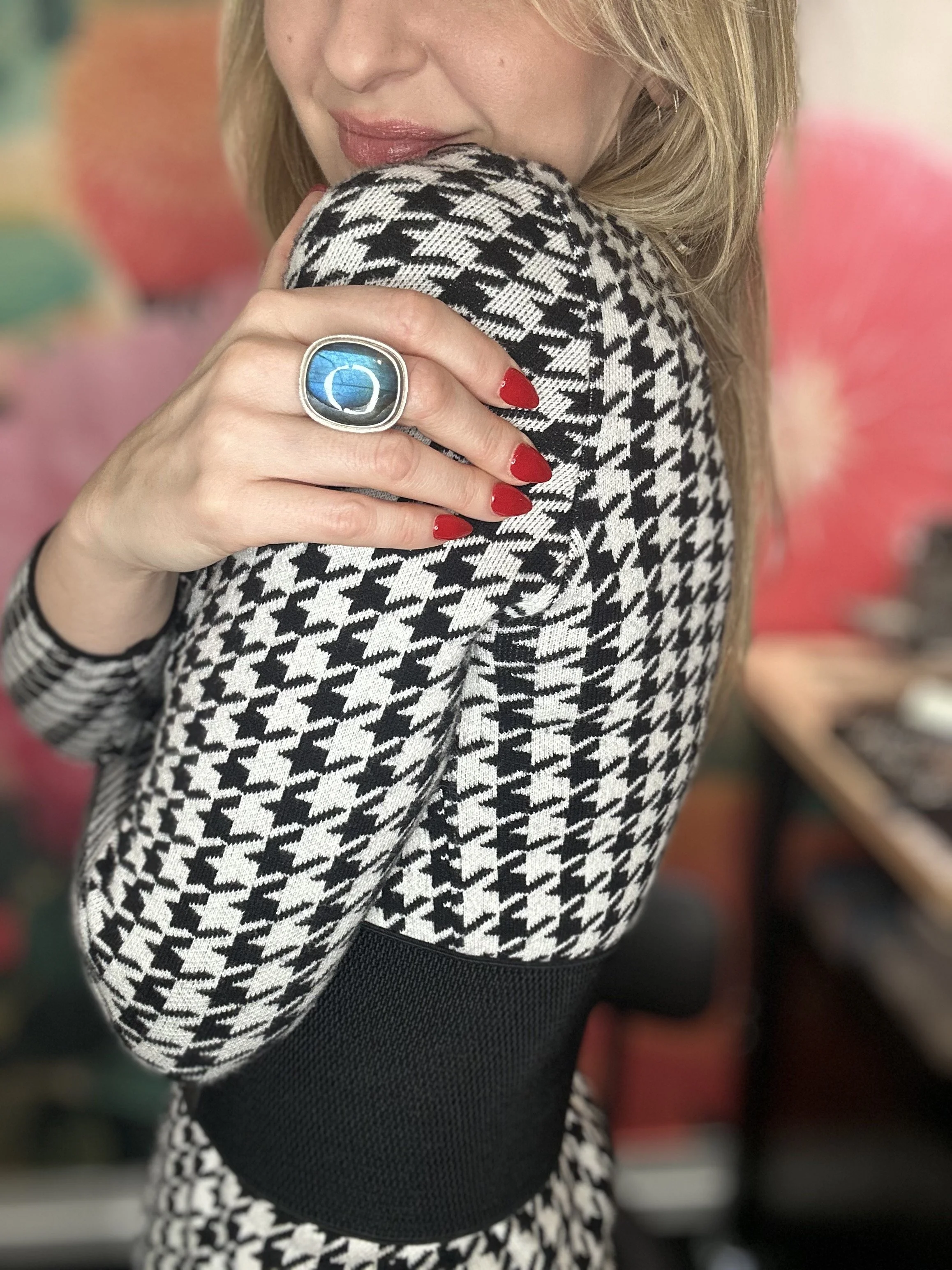 Blonde woman in black and white houndstooth sweater models a large blue labradorite stone ring in a silver cabochon.