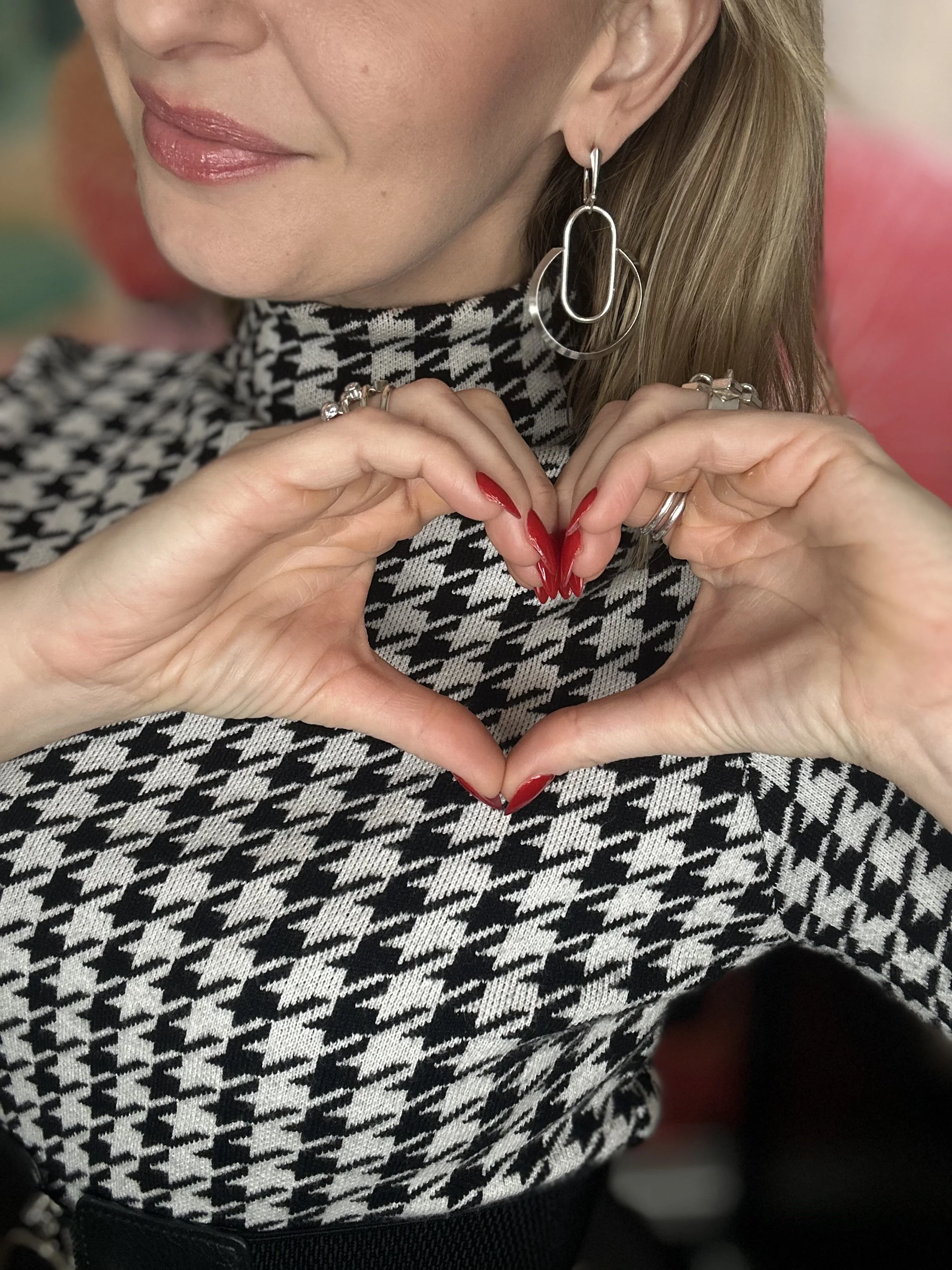 Blonde model makes heart shape with her hands as she showcases silver Geo Hoop earrings.