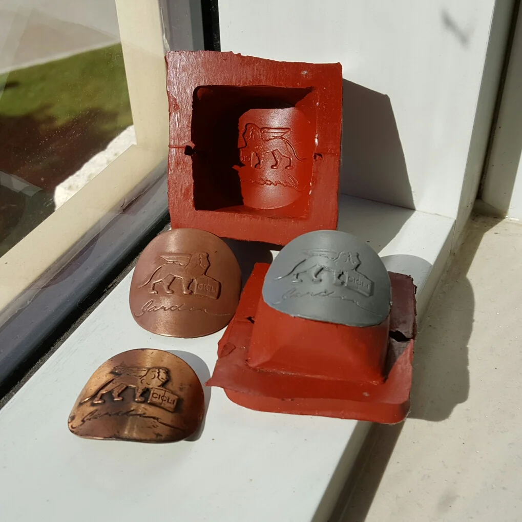 The mold, the copper badge, a fresh aluminium badge, and an original. At first I was a little disappointed because I couldn't get the reproductions to be as bright as the electroplated copper, but I think I'm OK with it. Electroplated copper is alwa…