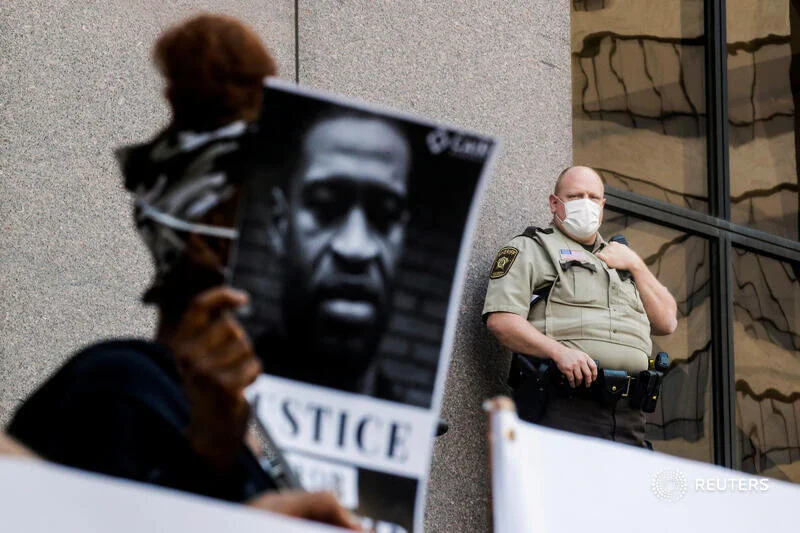  A police officer wearing a face mask looks on while protesters gather outside the city hall after a white police officer was caught on a bystander's video pressing his knee into the neck of African-American man George Floyd, who later died at a hosp