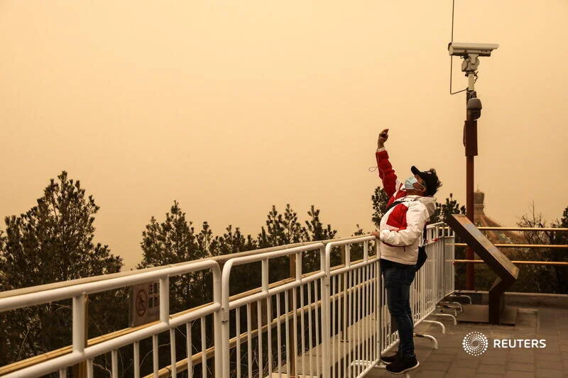  A visitor wearing a face mask stands on barricades at a peak overlooking the Forbidden City at Jingshan Park, as the city is hit by sandstorm, in Beijing, China March 15, 2021. REUTERS/Tingshu Wang 