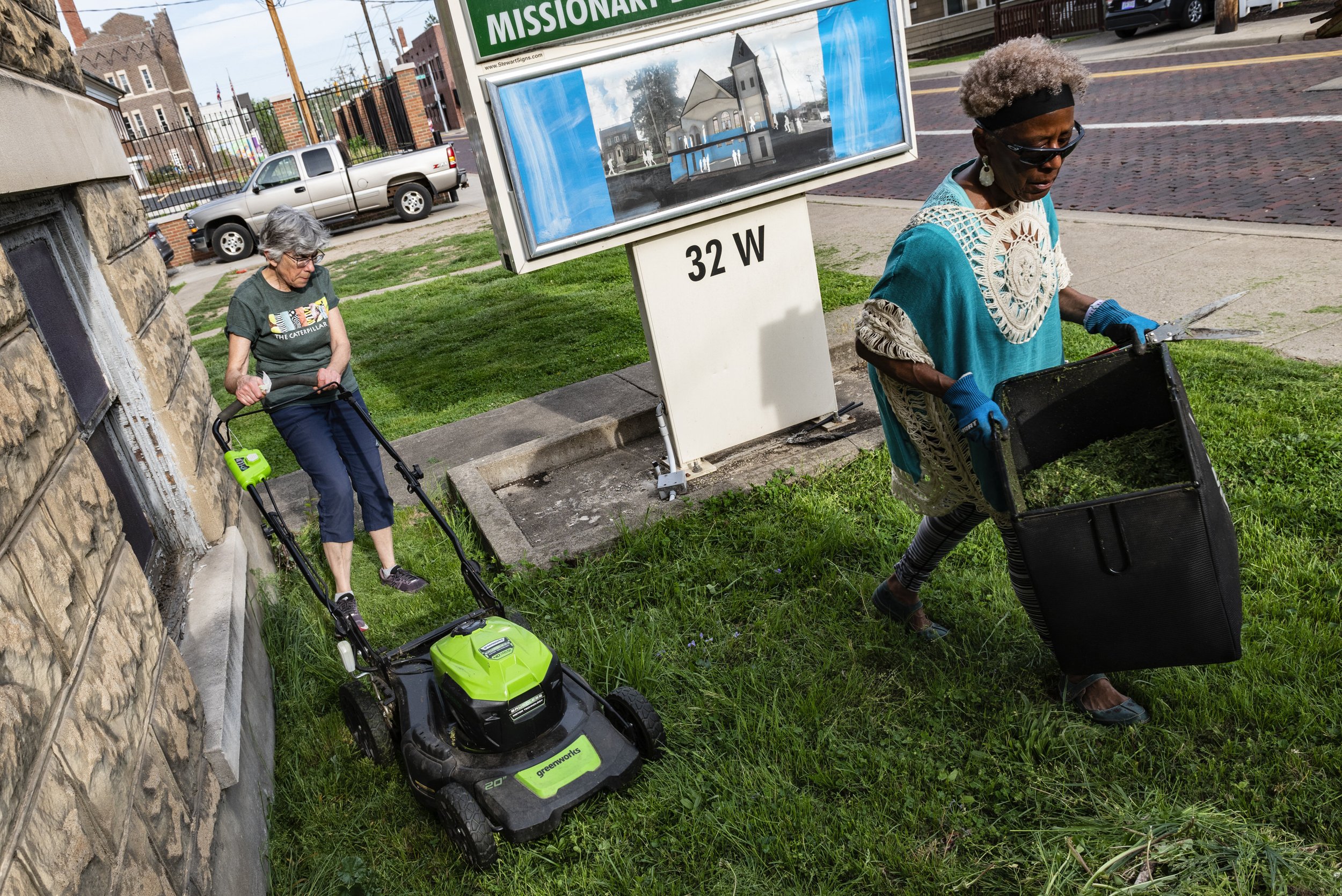  Dr. Tee Ford-Ahmed walks off with a container of weeds and grass while her friend and fellow Mount Zion Baptist Church Preservation Society member Dr. Susan Righi continues to mow the grass outside Mount Zion Baptist Church in Athens, Ohio, Thursday