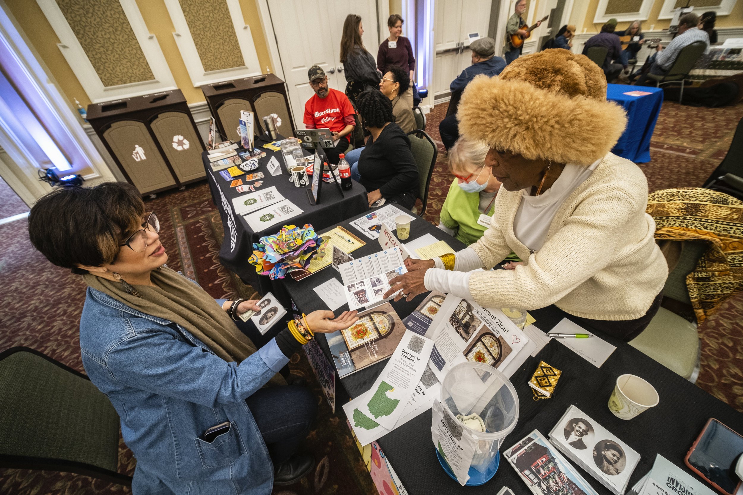  Dr. Tee Ford-Ahmed hands Affrilachian artist Crystal Good a brochure narrating the history of noteworthy Black Americans that lived in Athens county at the Mount Zion Baptist Church Preservation Society's booth during AppalachiaFest in Ohio Universi