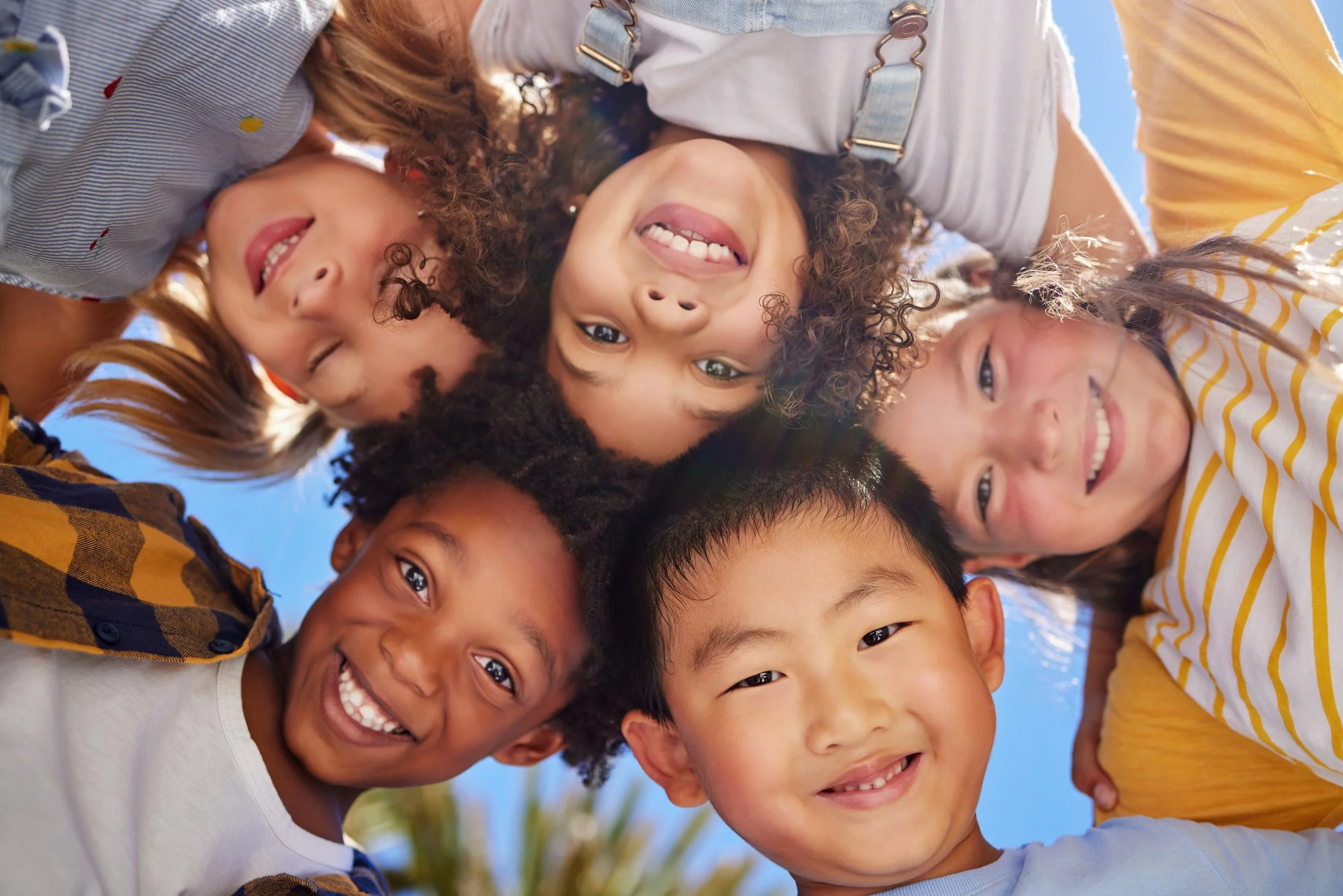 A group of diverse children looking down at the camera in a circle outdoors.
