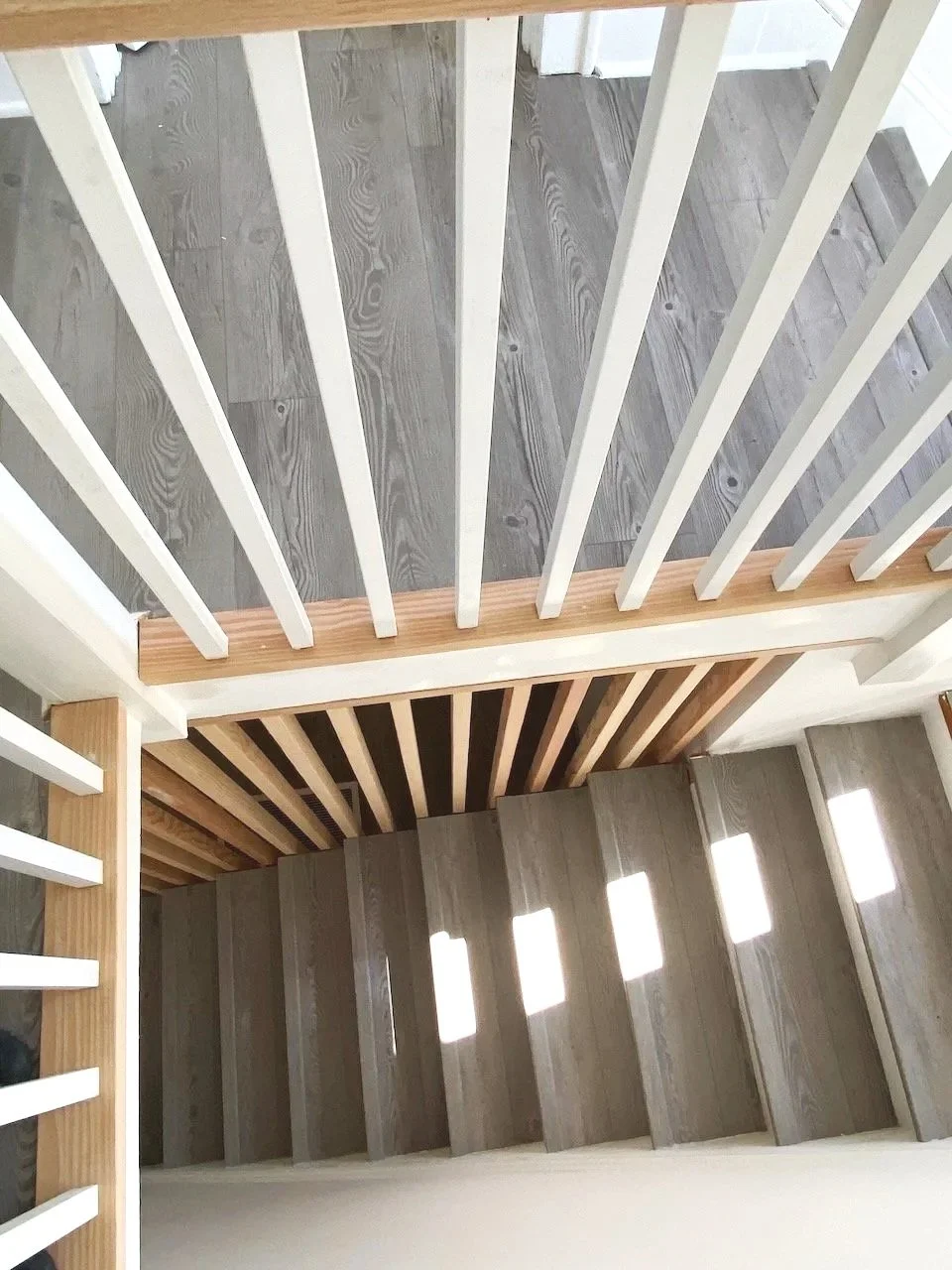 View of a renovated staircase with new wood steps, painted white ballustrade and natural wood partition wall
