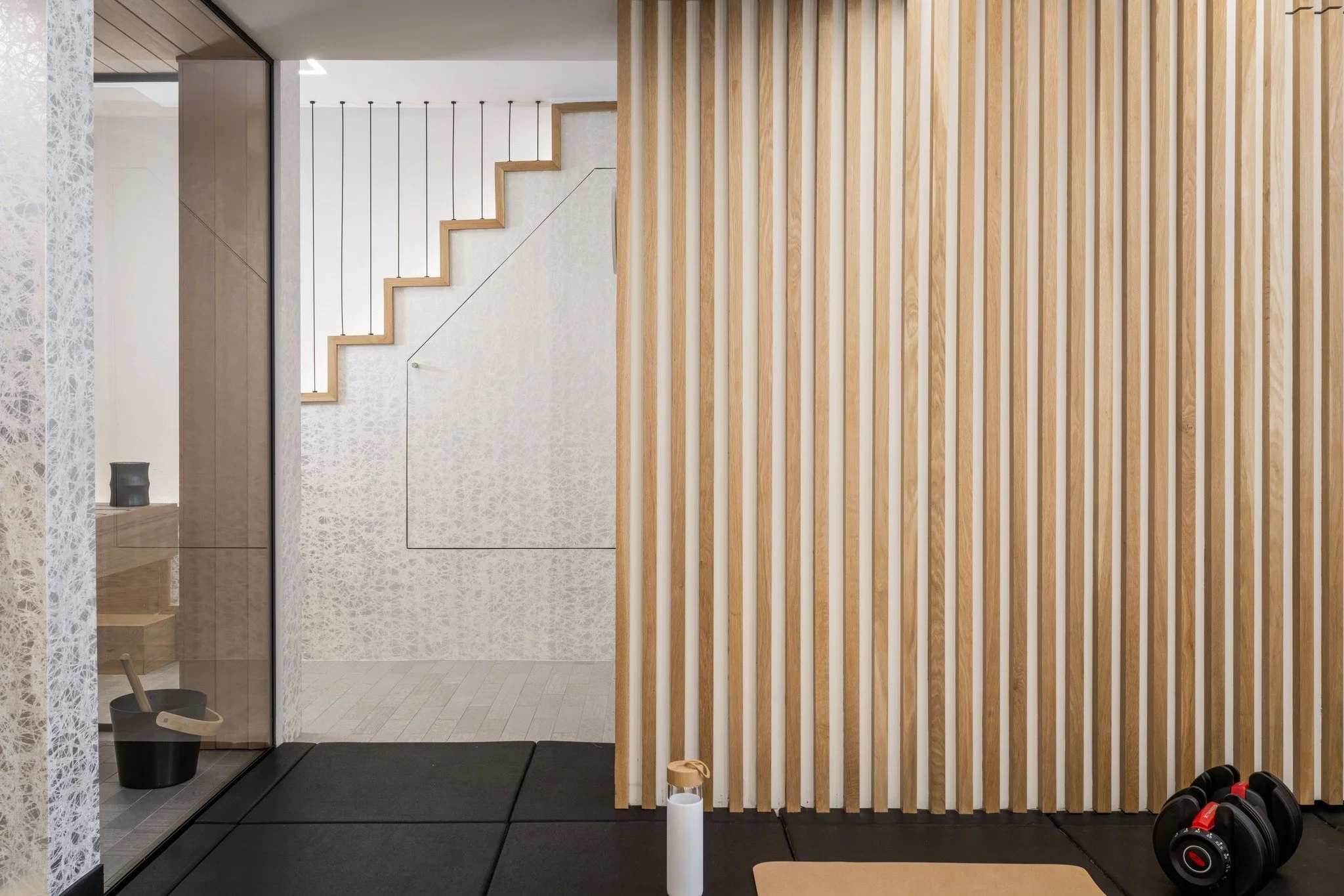 Form meets function in our Home Health Haven project. This clever under-stair design conceals fitness gear behind a custom door clad in the same patterned wall treatment, maintaining a seamless aesthetic. It’s a reminder that wellness spaces ca