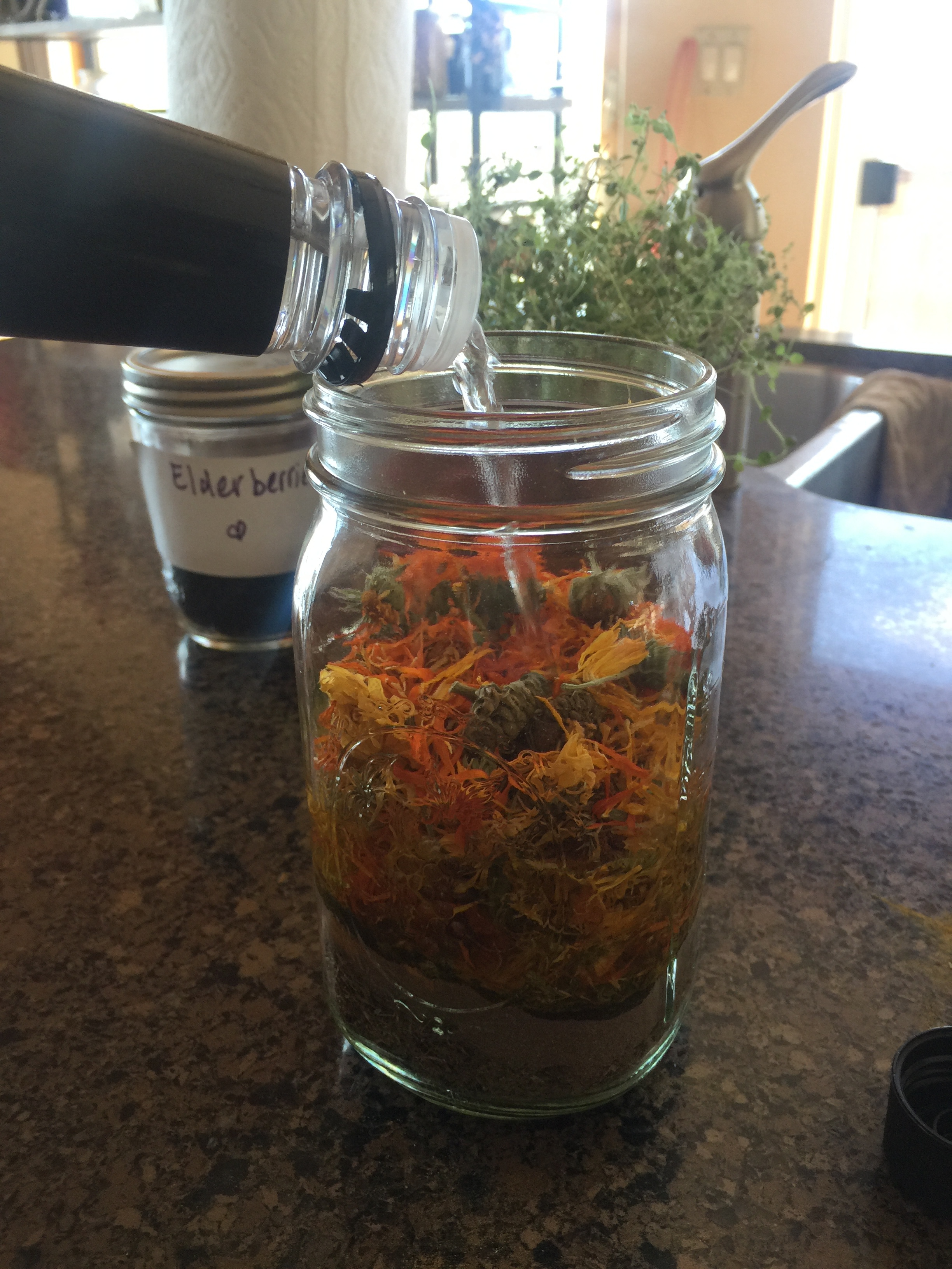 Pouring the alcohol over the herbs. Give a little shake, then pour a bit more, until the herbs are saturated and the liquid is about an inch from the top.