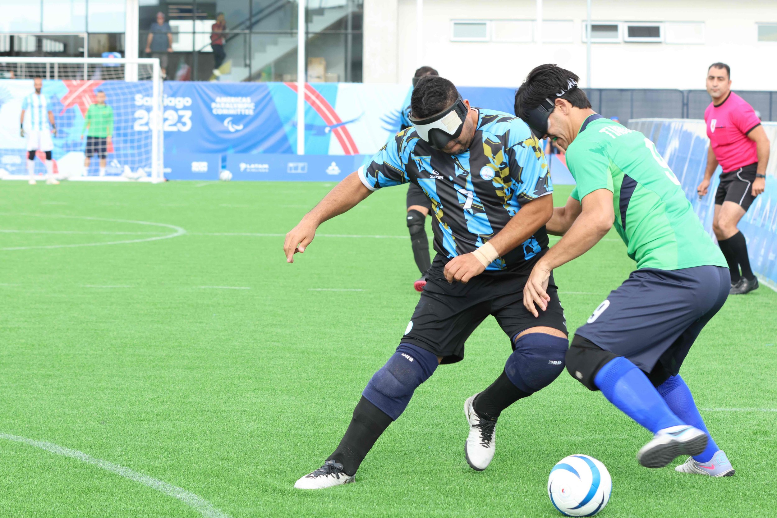 Two blind soccer players compete over a soccer ball in the middle of the field.