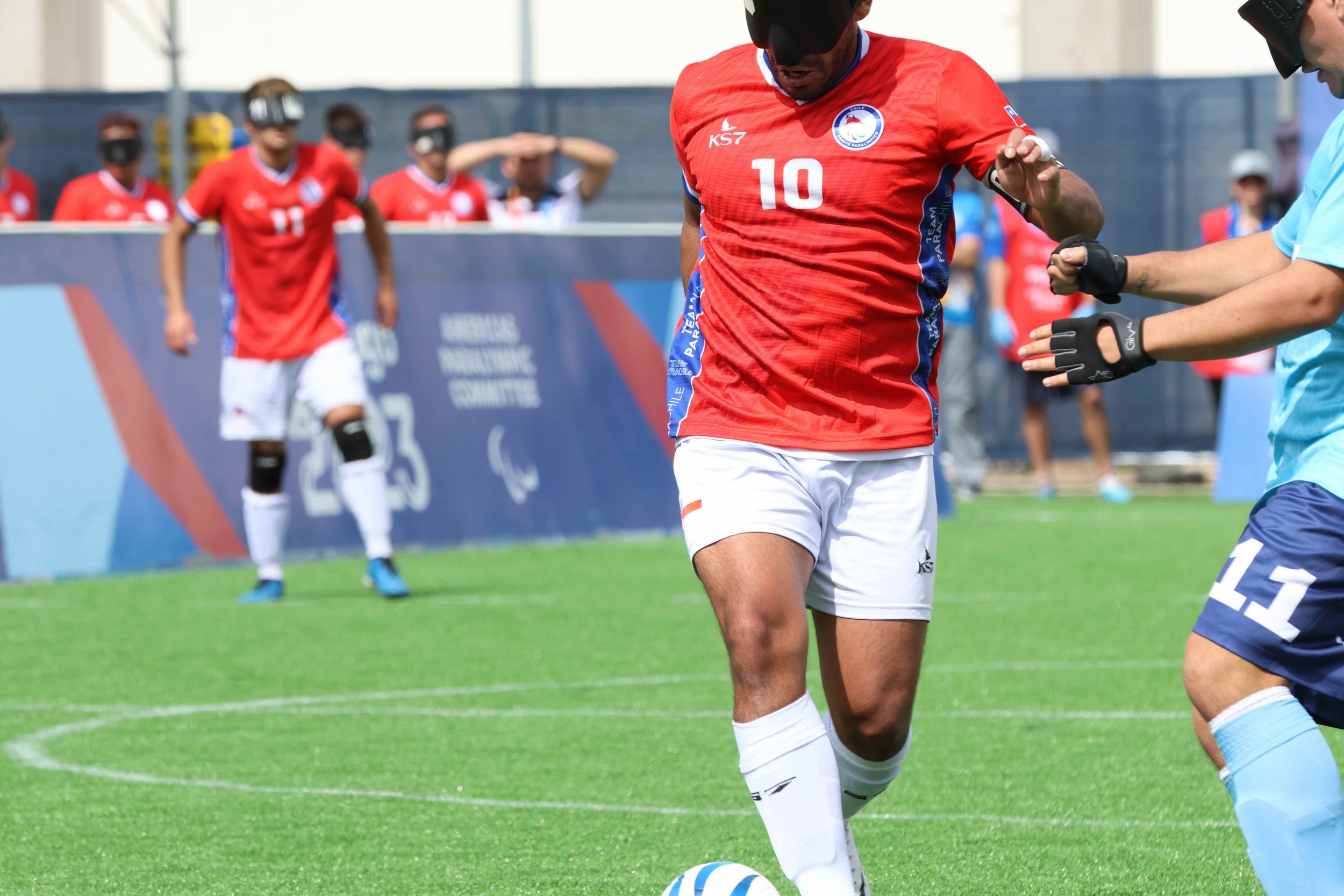 A blind soccer player runs down the field with a team mate following behind.