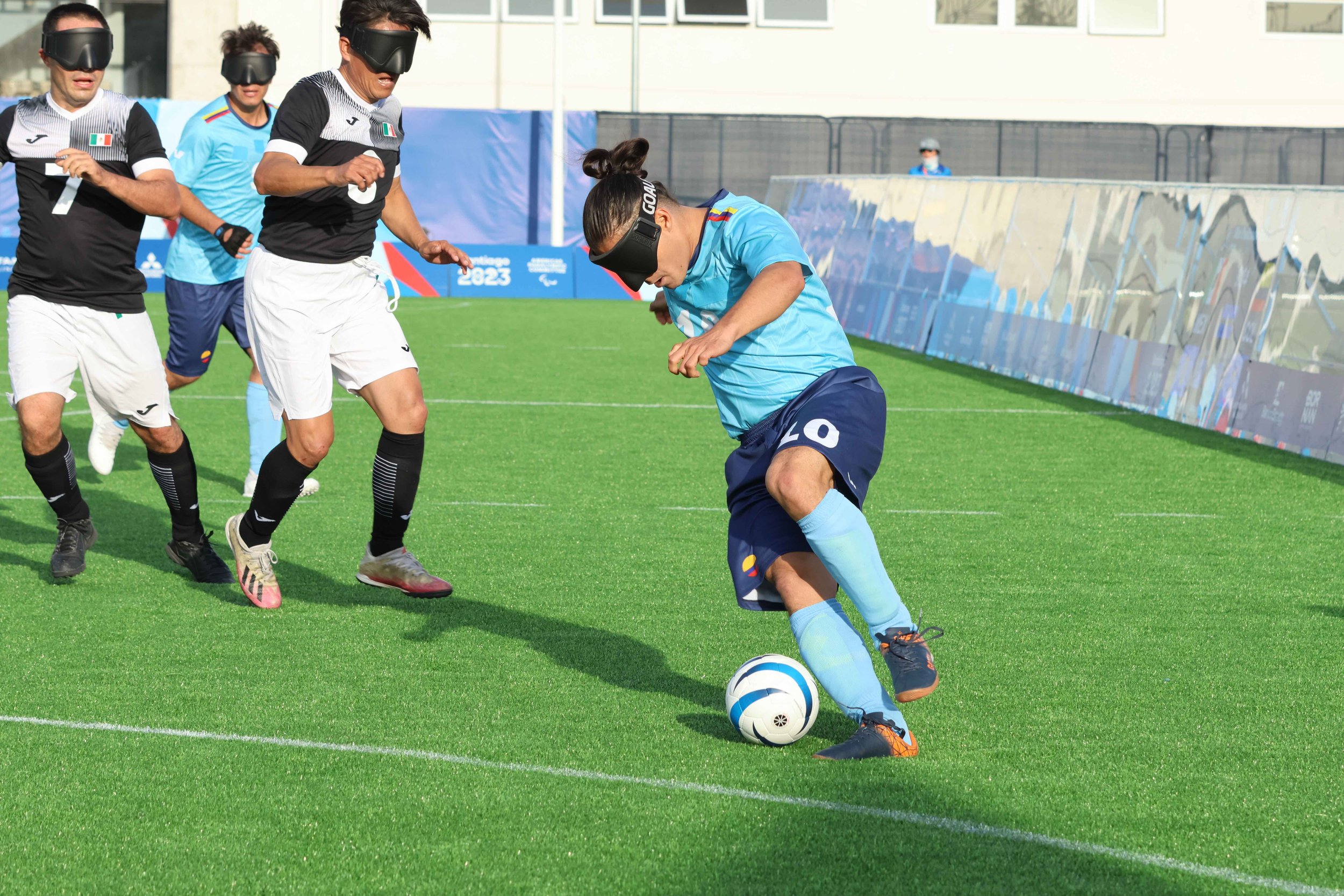 A blind soccer player dribbles a soccer ball down the field while opposing players approach from the side.