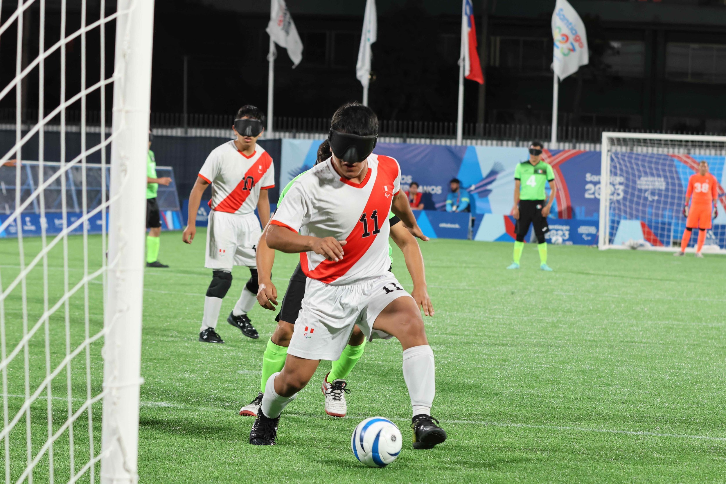 A blind soccer players dribbles the soccer ball towards the goal as players follow shortly behind.