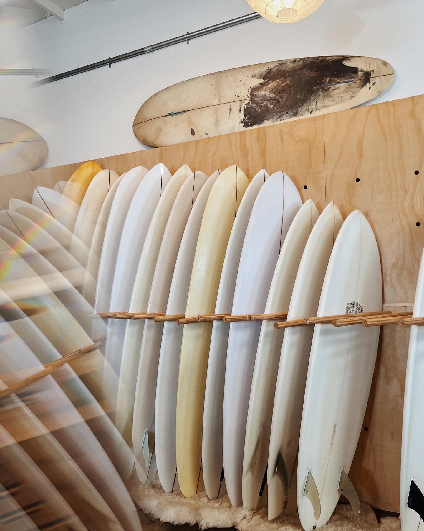 Multiple surfboards of various shapes and sizes stored vertically on a rack in a surf shop with additional surfboards mounted on the wall.
