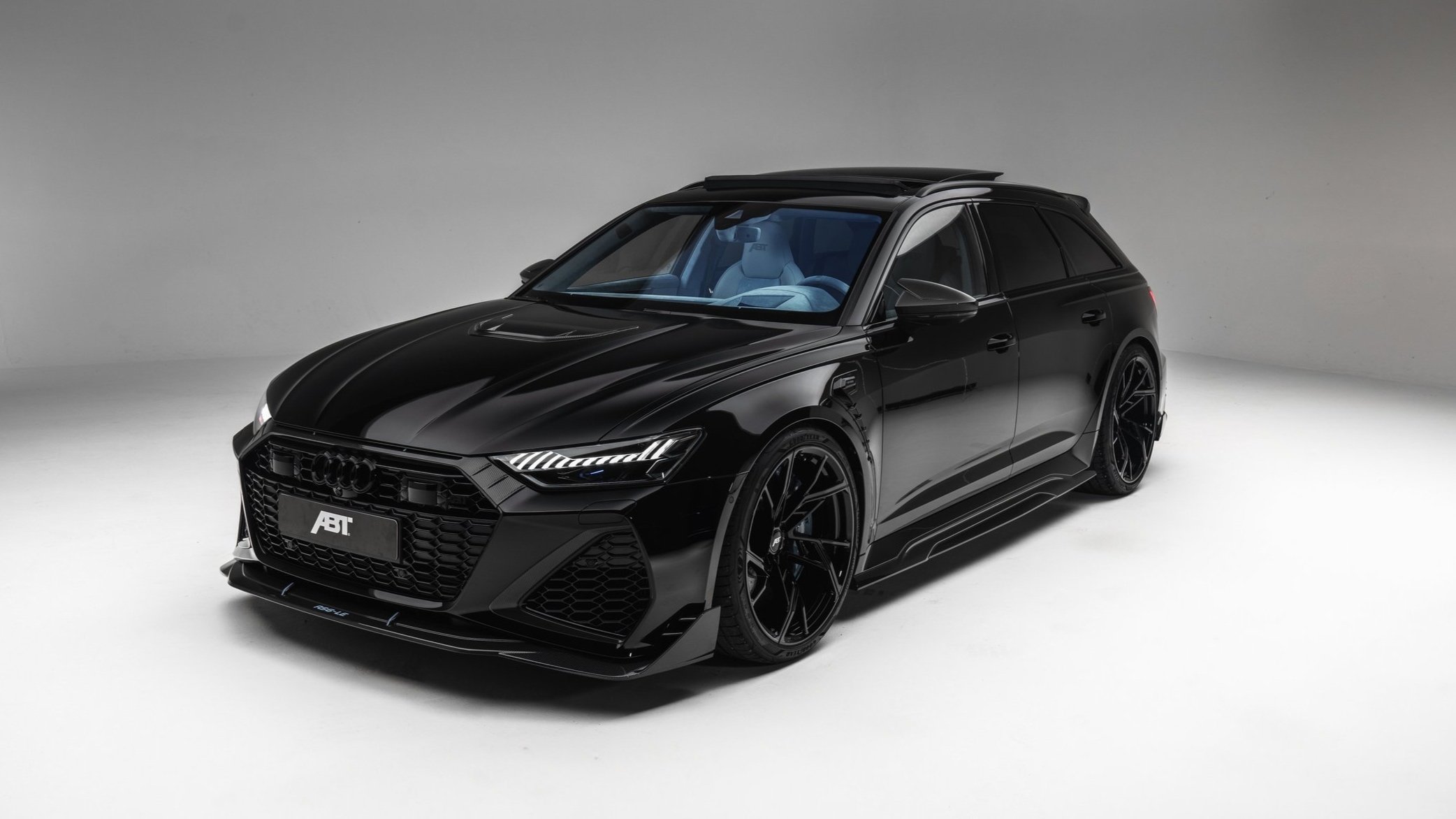 A sleek black Audi car with custom ABT parts and large sporty wheels in a photography studio setting.