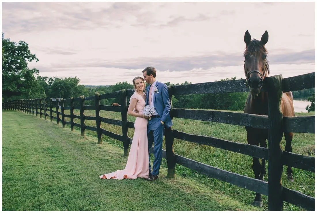 A bride and groom standing next to a horse in beautiful green pastures