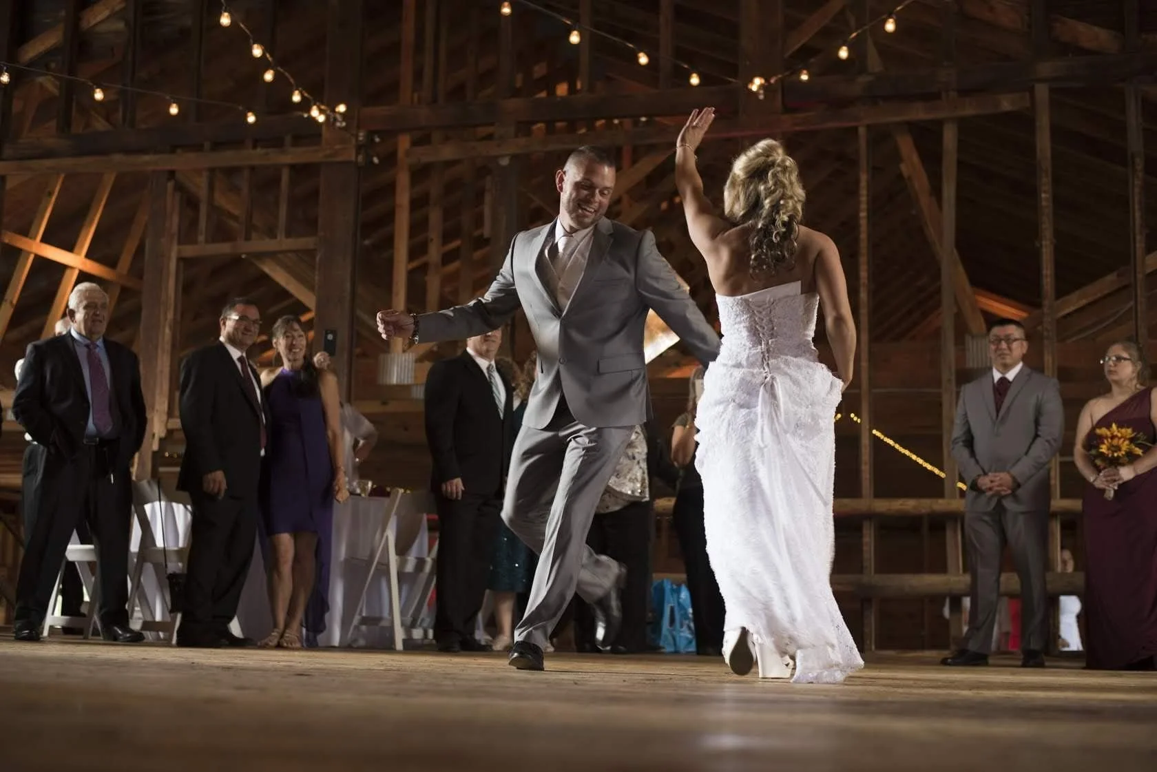 Bride and groom dancing at their rustic barn wedding reception with charming fairy lights above