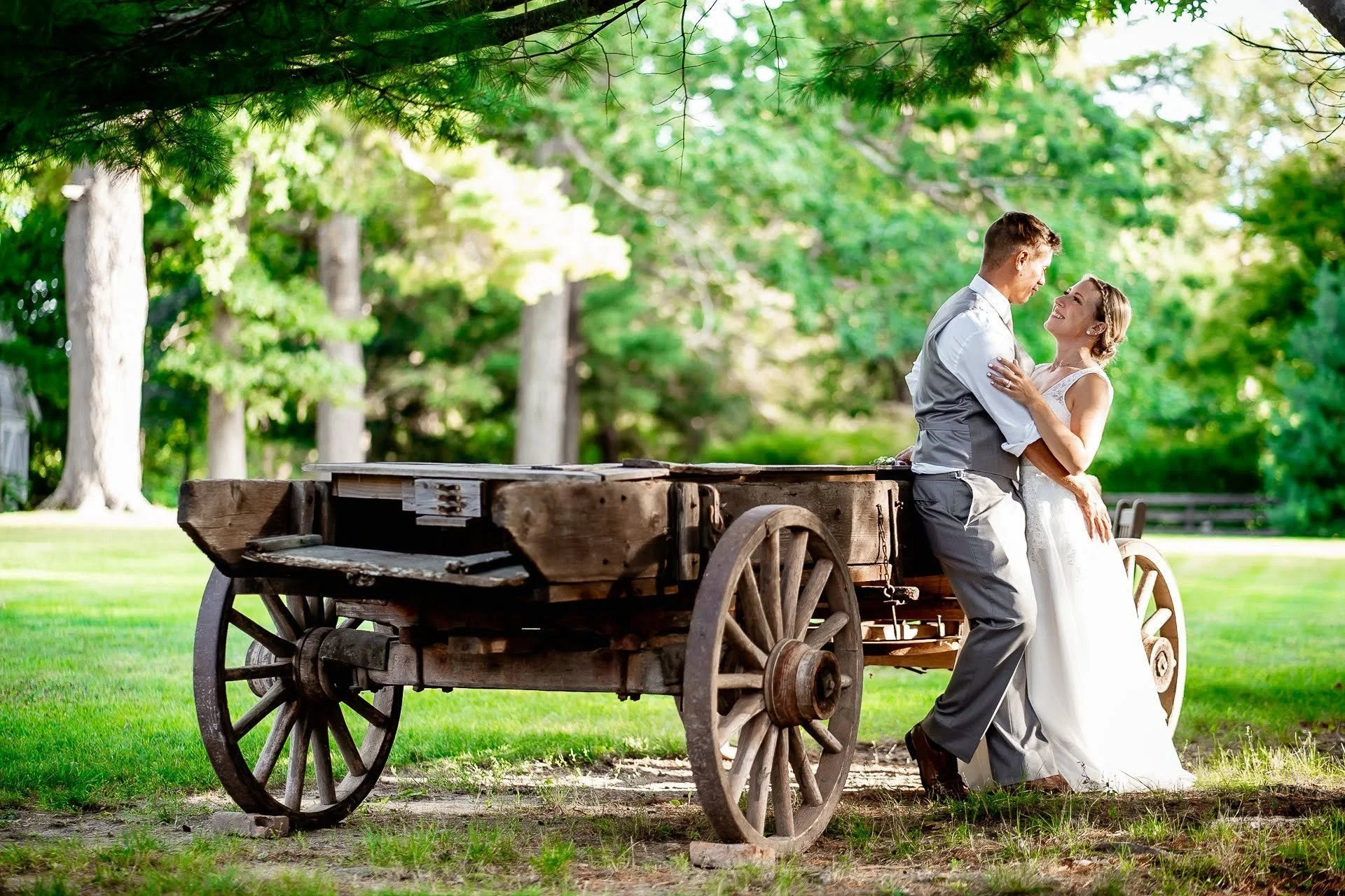 Bride and groom outside in the lush green grounds, leaning against an old-fashioned cart