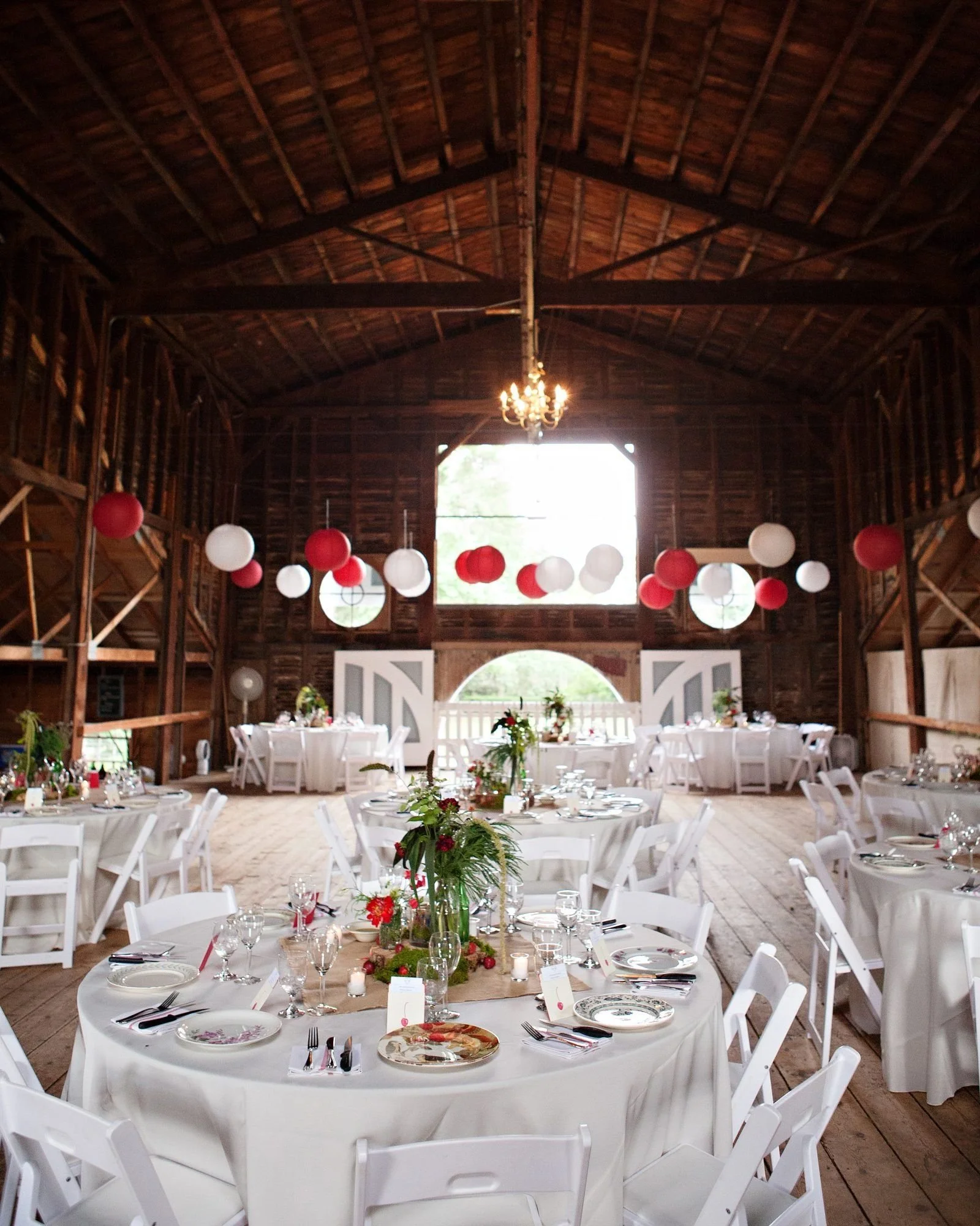 An unforgettable wedding reception in a barn with white tables and red lanterns.