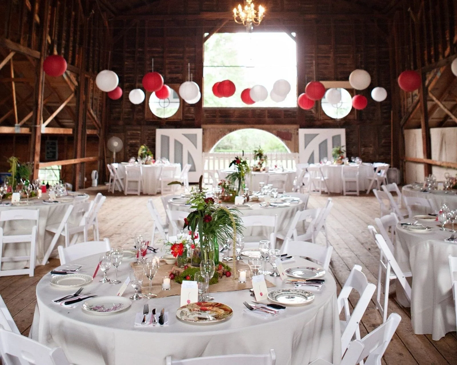 Eclectic barn wedding decorations with red and white laterns and white set reception tables